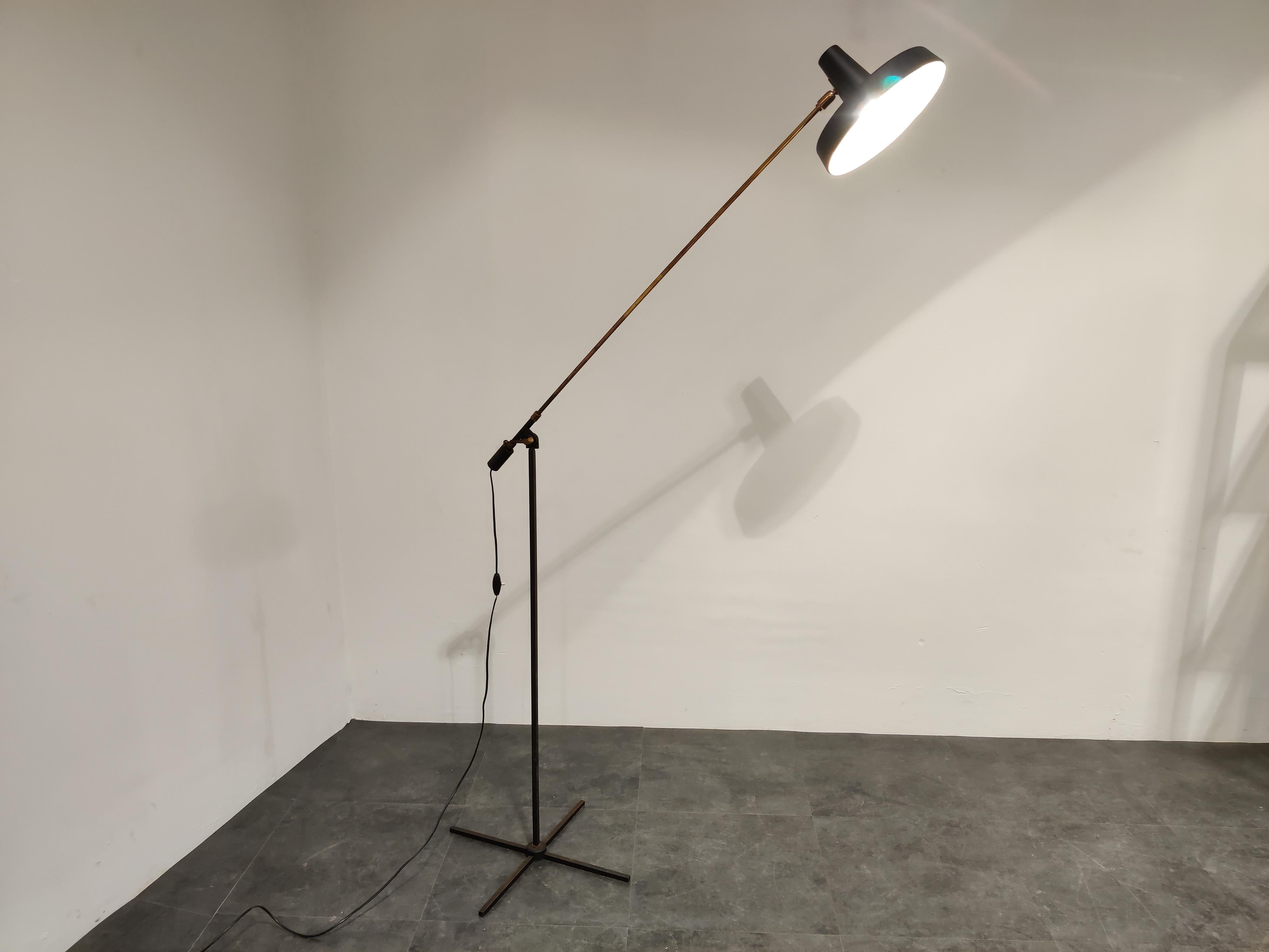 Elegant midcentury articulated floor lamp made of brass and a X shaped base.

The shade has an enameled layer on the inside to create a soft light. The outer side of the lamp shade is made of aluminum mounted an a brass arm.

Both shade and arm
