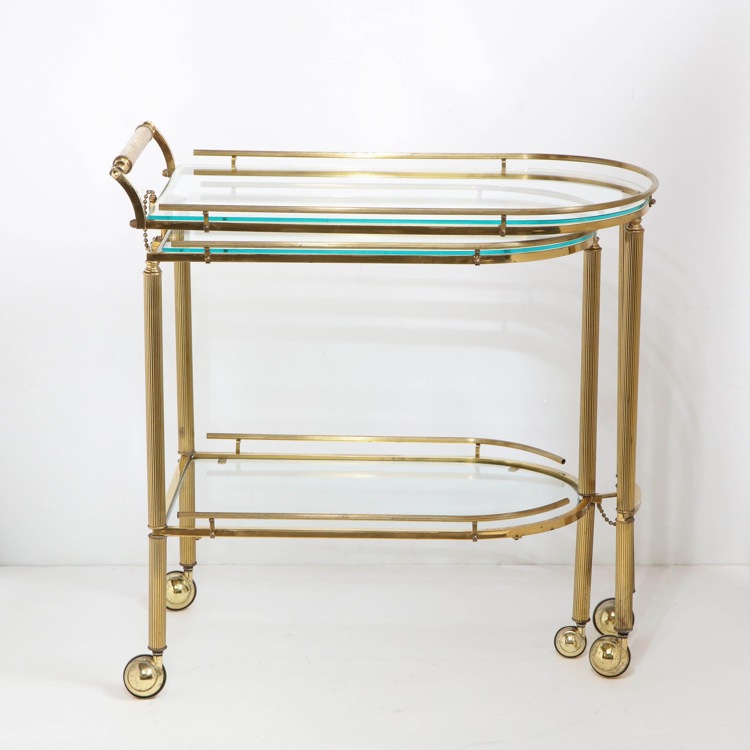 This refined Mid-Century Modern three tier articulating brass bar cart was realized in the United States, circa 1970. It features a bullet form silhouette consisting of two articulating demilune shaped tiers with translucent glass centers, that