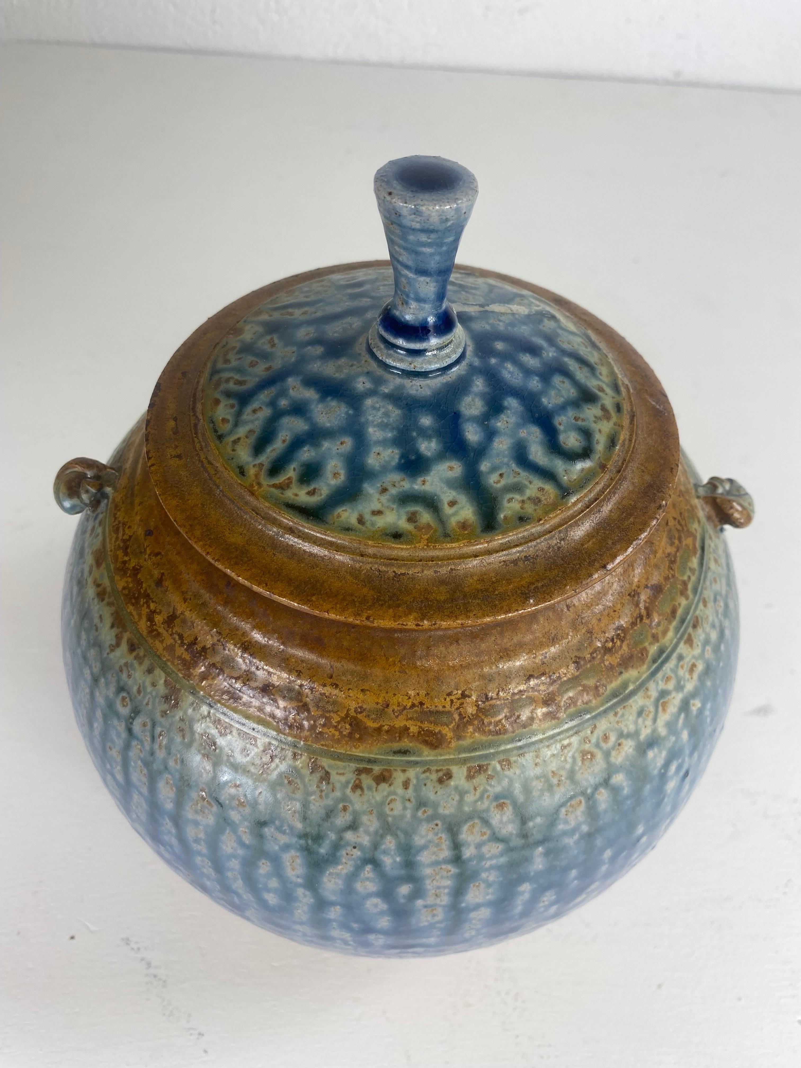 Il s'agit d'un bol en poterie artisanale vintage du milieu du siècle avec couvercle. Cette poterie artisanale présente un glaçage bleu œuf de robin et marron unique et distinctif, avec une finition antique à l'extérieur. Le bol est muni de deux