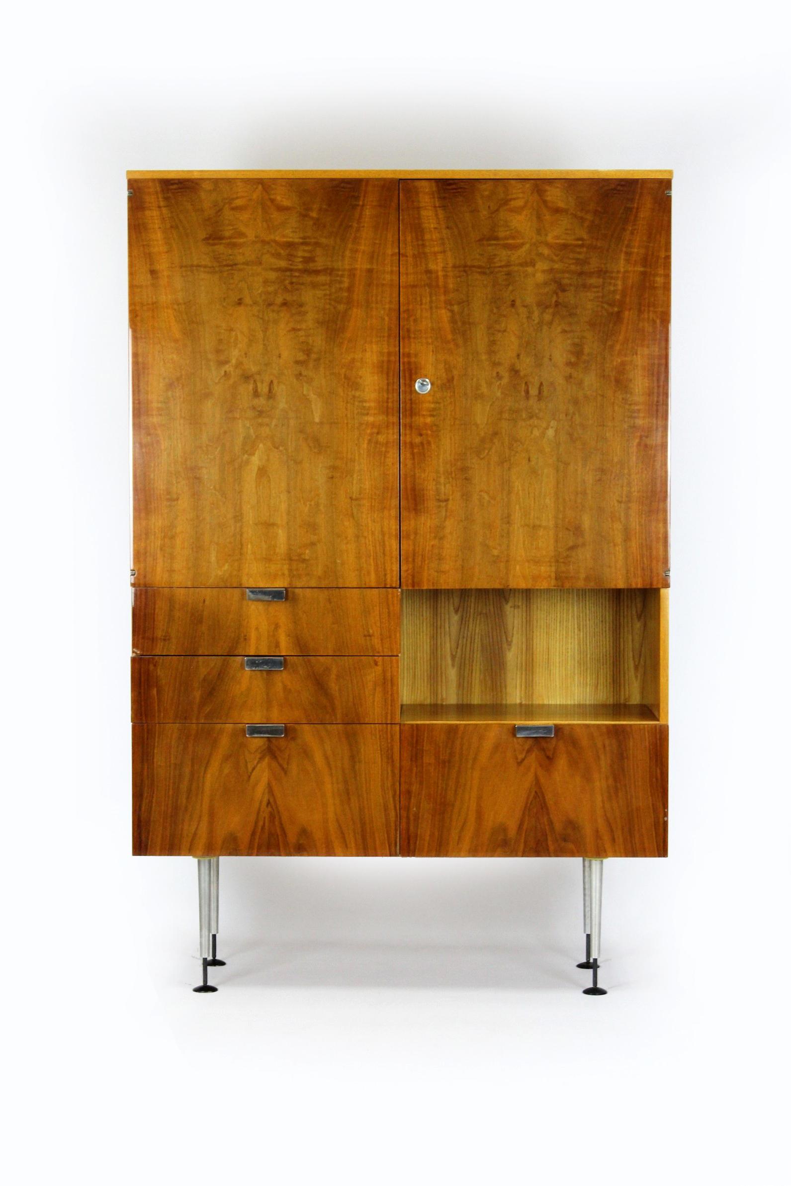 This Mid-Century Modern wardrobe from the 1960s was manufactured by Jiton in the Czech Republic. The wardrobe is made of two types of wood - ash and walnut. The wardrobe has original glass shelves and drawers. Supported on height-adjustable metal