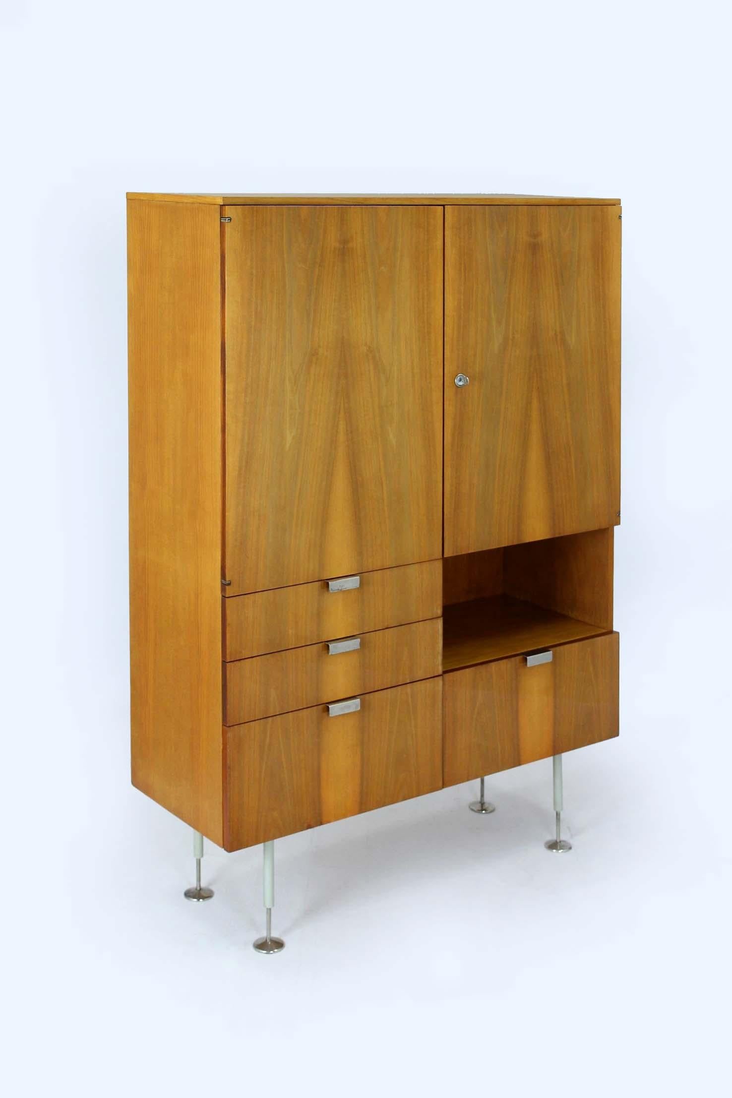 
Cette armoire moderne du milieu du siècle dernier, datant des années 1960, a été fabriquée par Jiton en République tchèque. L'armoire est fabriquée en deux types de bois : le frêne et le noyer. L'armoire possède des étagères et des tiroirs en verre