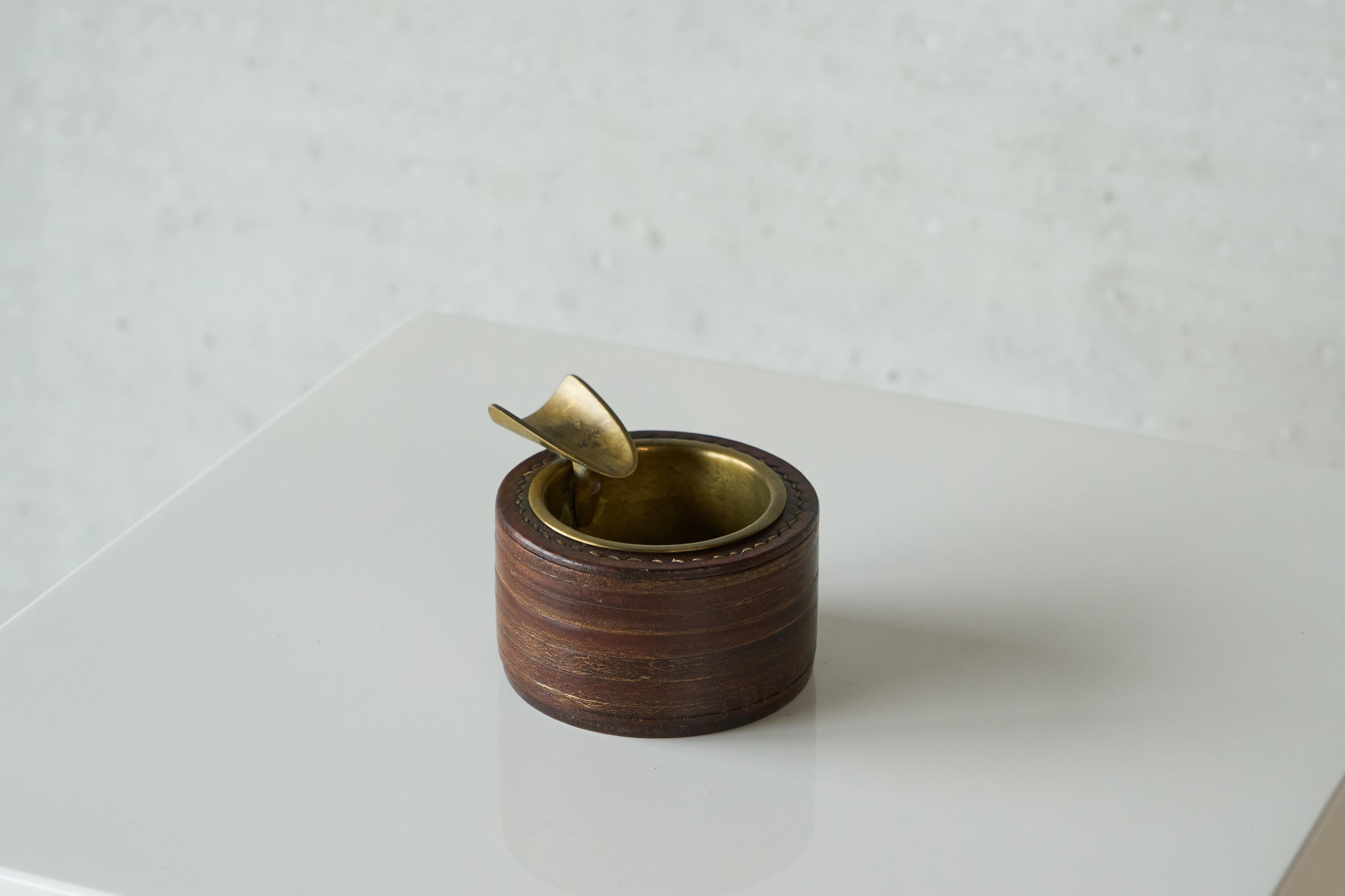 Posacenere di metà secolo in pelle e ottone patinato, Europa, anni '60.

Si tratta di un bellissimo posacenere di metà secolo in pelle e ottone patinato. Il design è ottimo: pelle marrone scuro con cuciture eleganti e un contenitore separato in