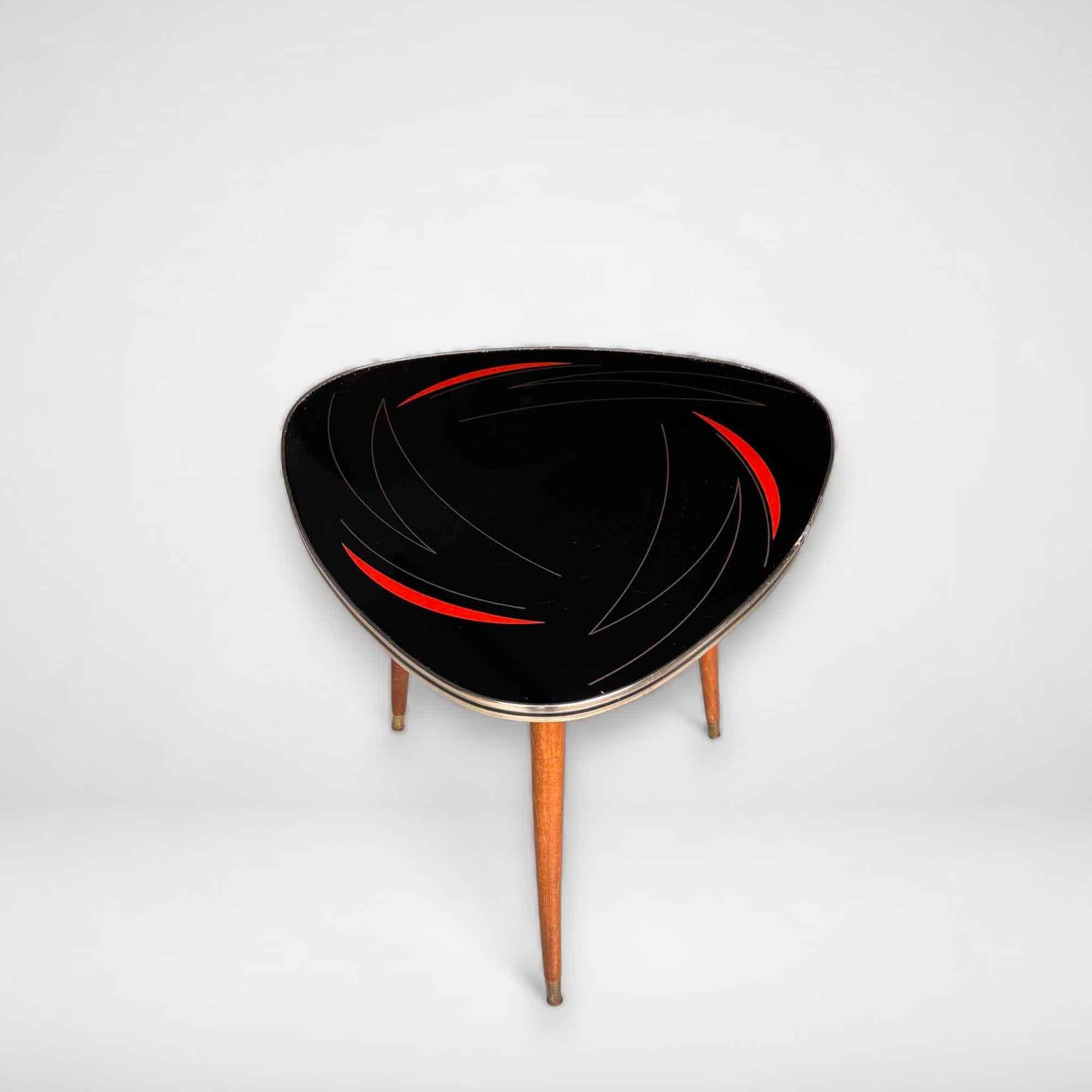 A beautiful fifties coffee table with an illustration in gold and red on a black background. This vintage table has the typical gold edge and stands on 3 sturdy wooden legs. The legs can be turned out. The style of this side table is also called