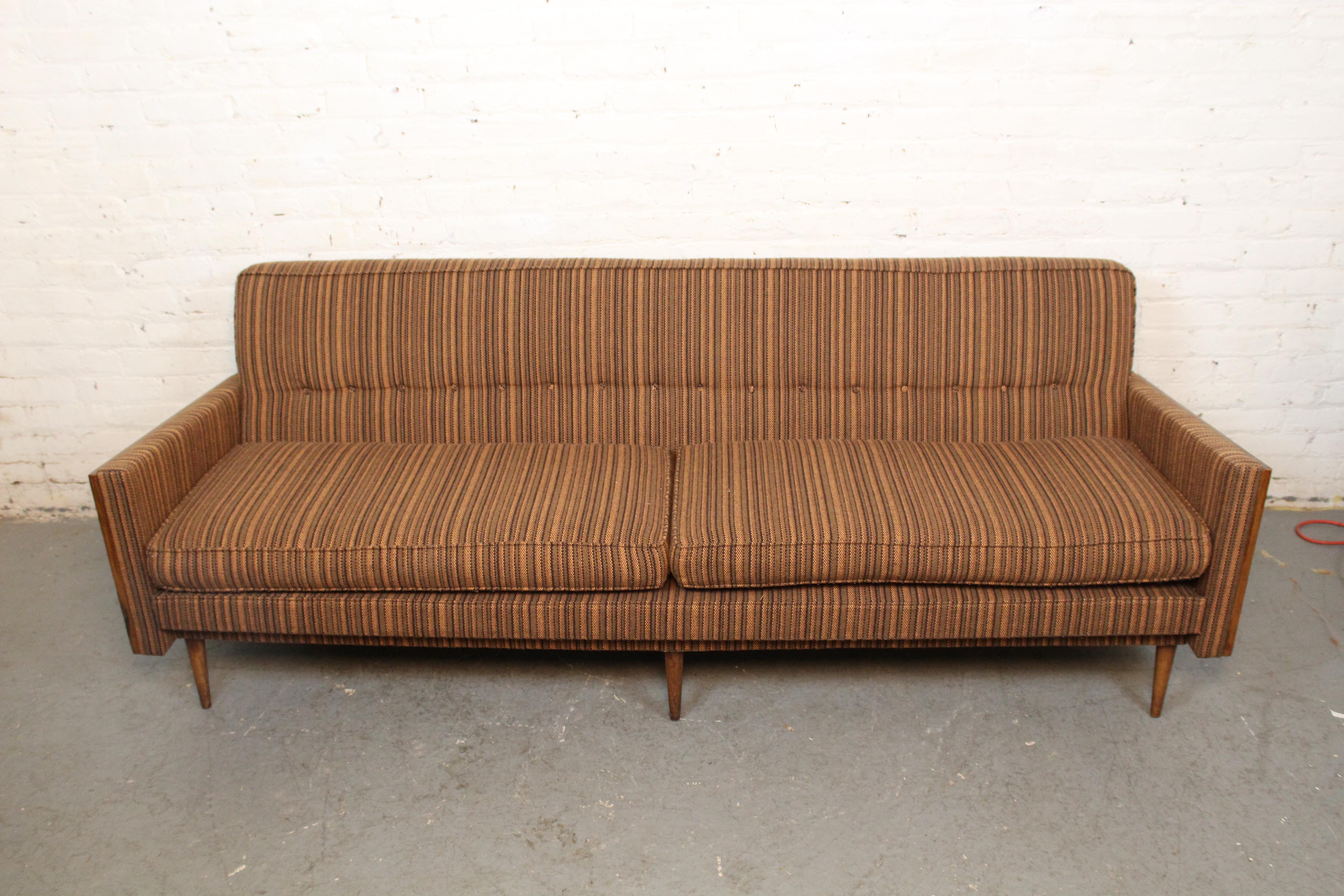 Versetzen Sie Ihr Wohnzimmer mit diesem fantastischen Sofa aus der Mitte des Jahrhunderts in eine andere Zeit! Dieses gemütliche Möbelstück in flippiger Atomzeitalter-Ästhetik zeichnet sich durch eine getuftete, gestreifte Tweed-Polsterung, eine