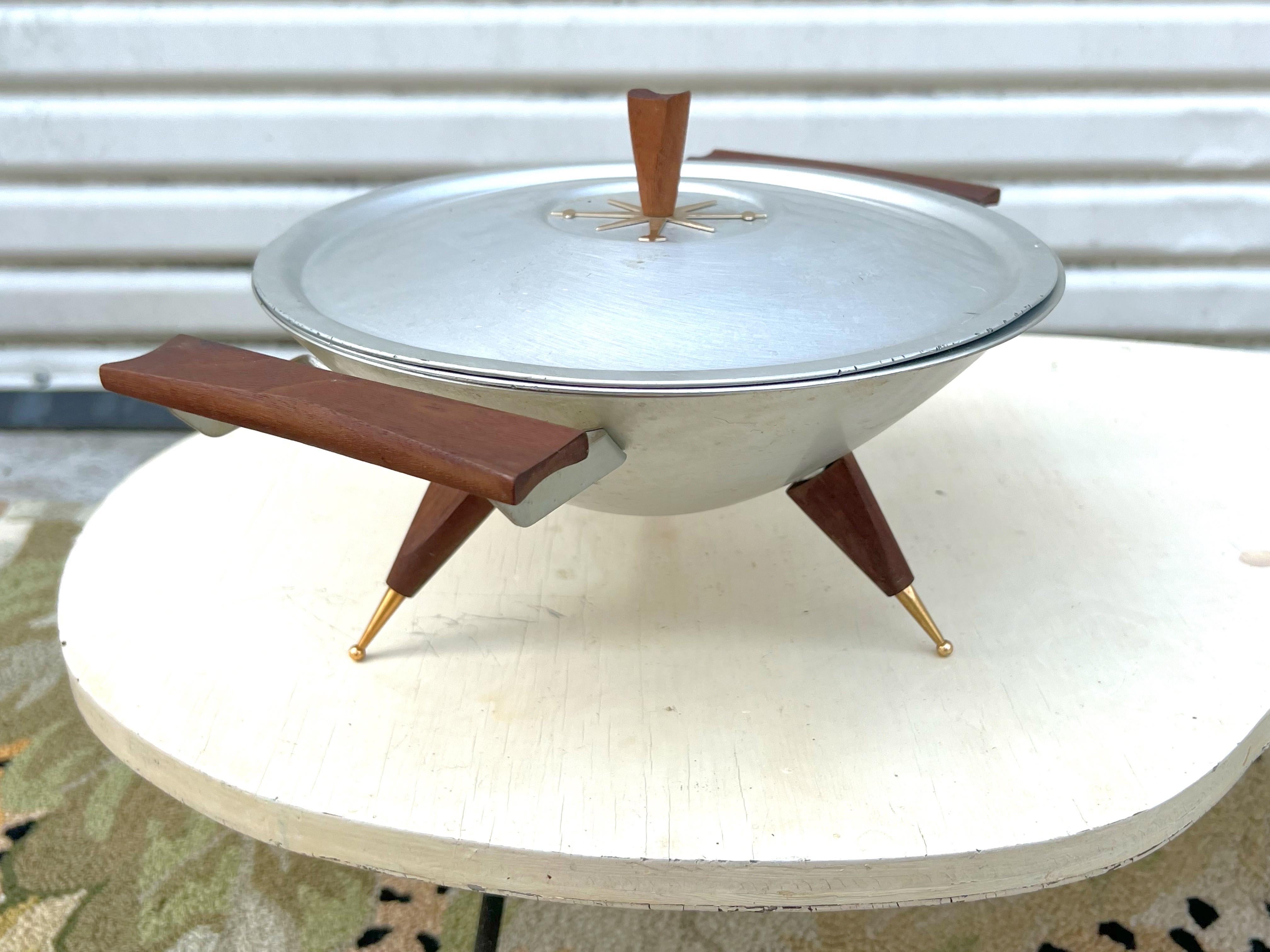 Jetsons for dinner. Aluminum and wood. Three pieces: bowl, lid, base. All nearly mint.   The wood and gold areas are in excellent condition. It would be a great serving piece for entertaining at parties or a decorative element in a room.