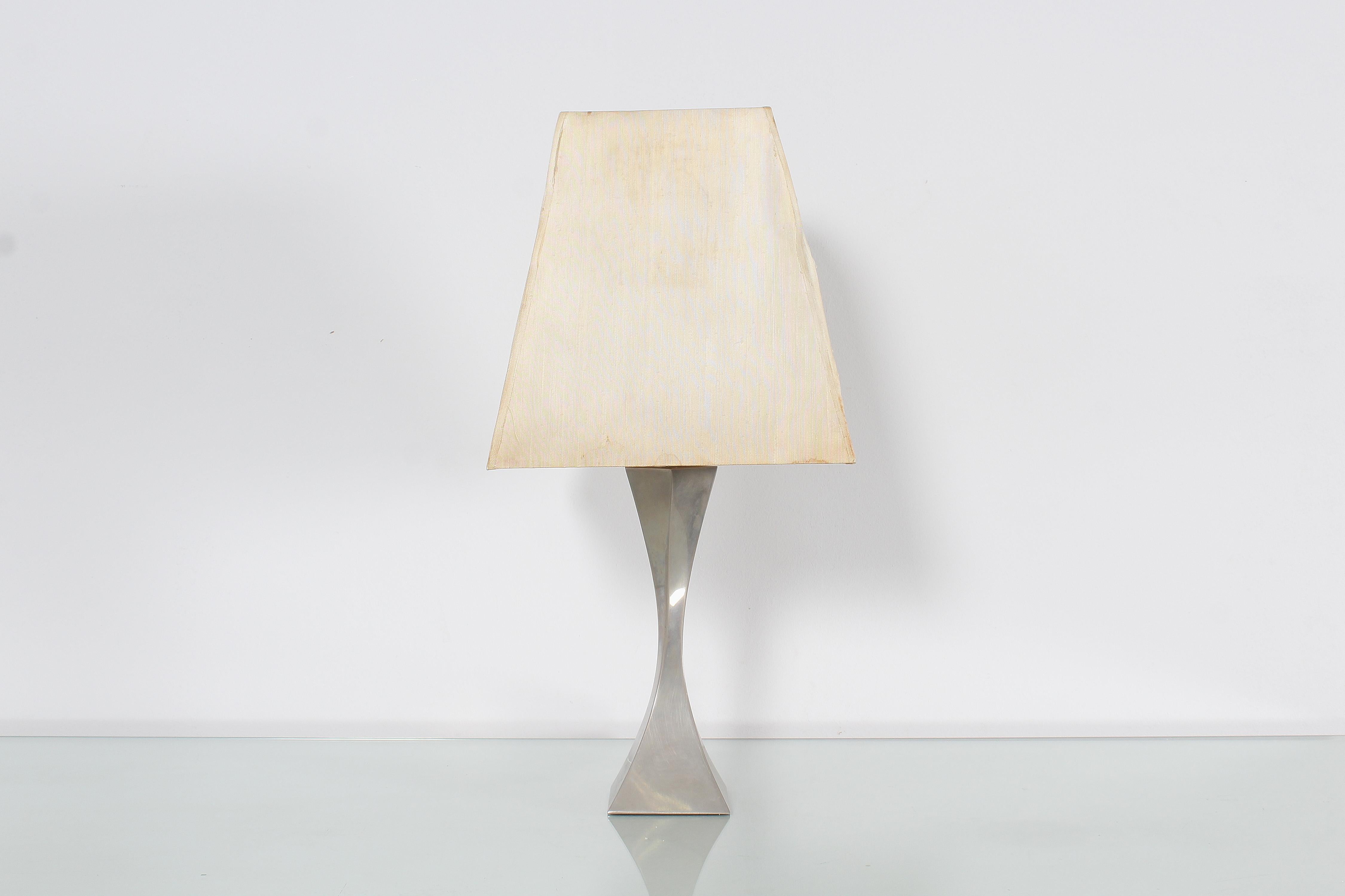 Stylish single light table lamp with nickel-plated brass base made up of two triangular pyramids, each slightly twisted, positioned head to head. Pyramidal lampshade in cream-white fabric with signs of wear. Attributed to A. Tonello e A. Montagna