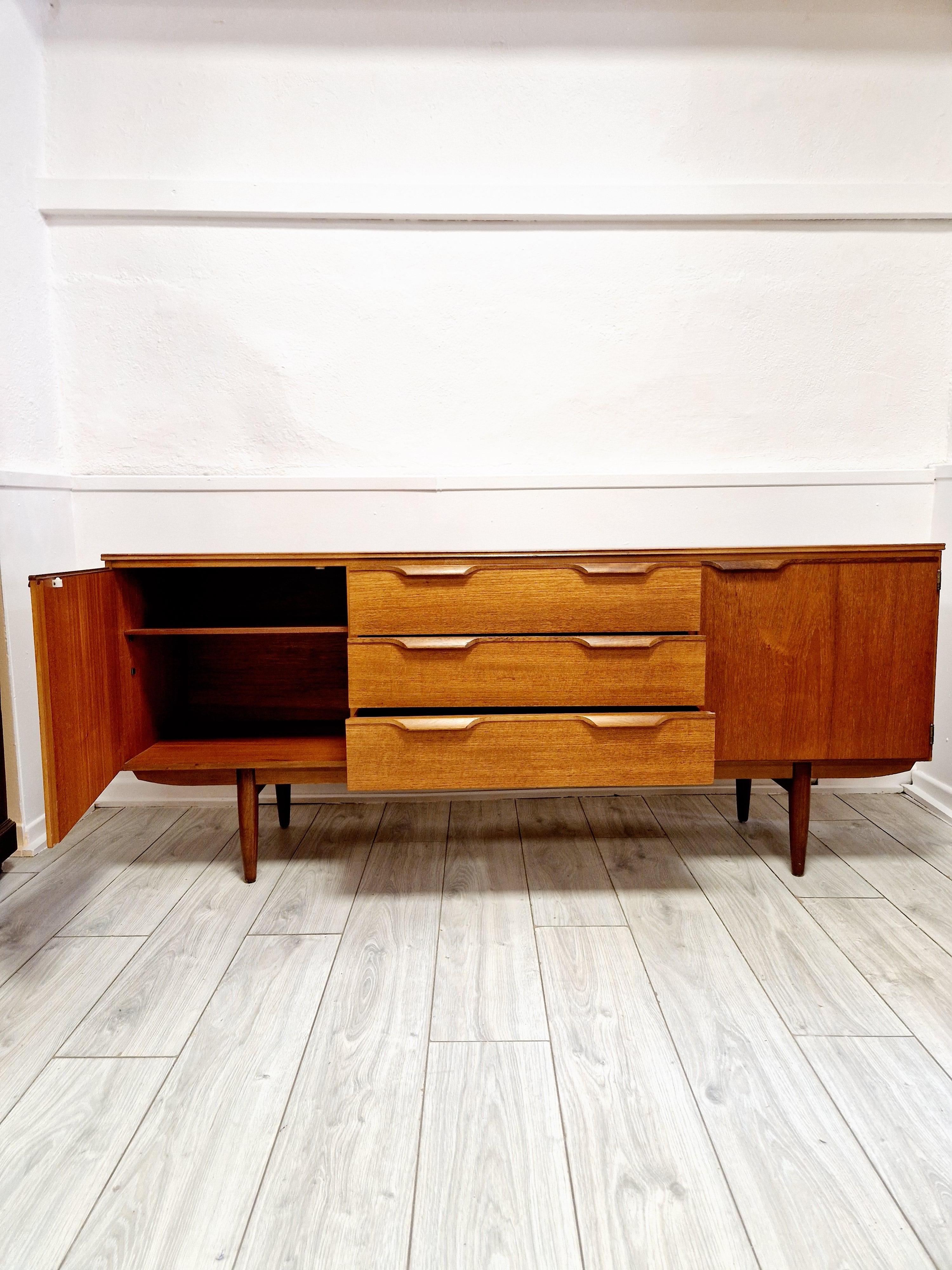 Scopri l'eleganza senza tempo della credenza in teak Mid Century Austinsuite, un'aggiunta straordinaria a qualsiasi ambiente. Realizzato con cura in Svezia, questo pezzo incarna la quintessenza del design moderno di metà secolo, con una ricca