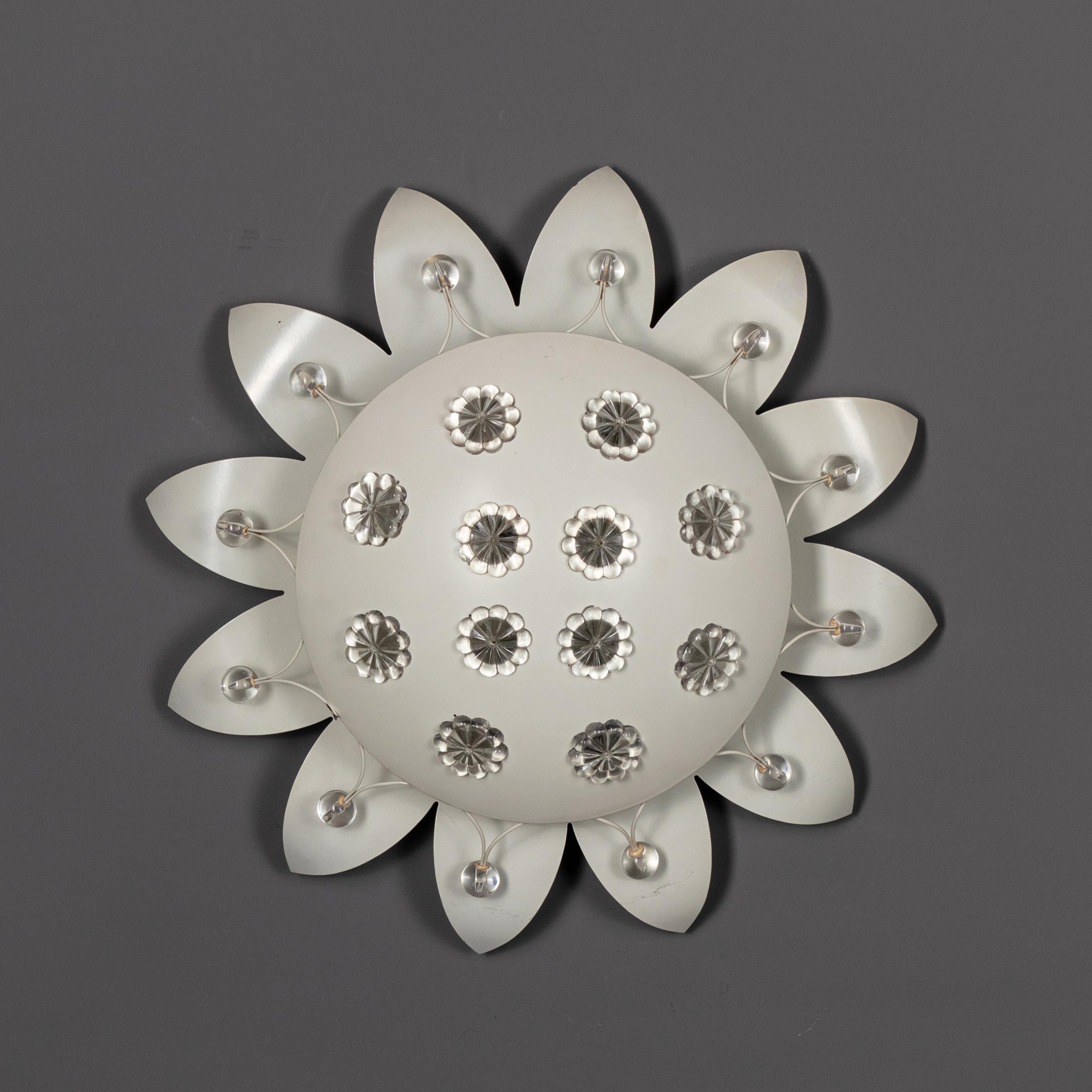 This Vienna sconce was designed by Emil Stejnar. A well known designer for his recognizable star-shaped designs in the 1950s.
White steel lacquered perforated shade with 10 small daisy flowers in the gaps, white wire steel rim with 12 faceted glass
