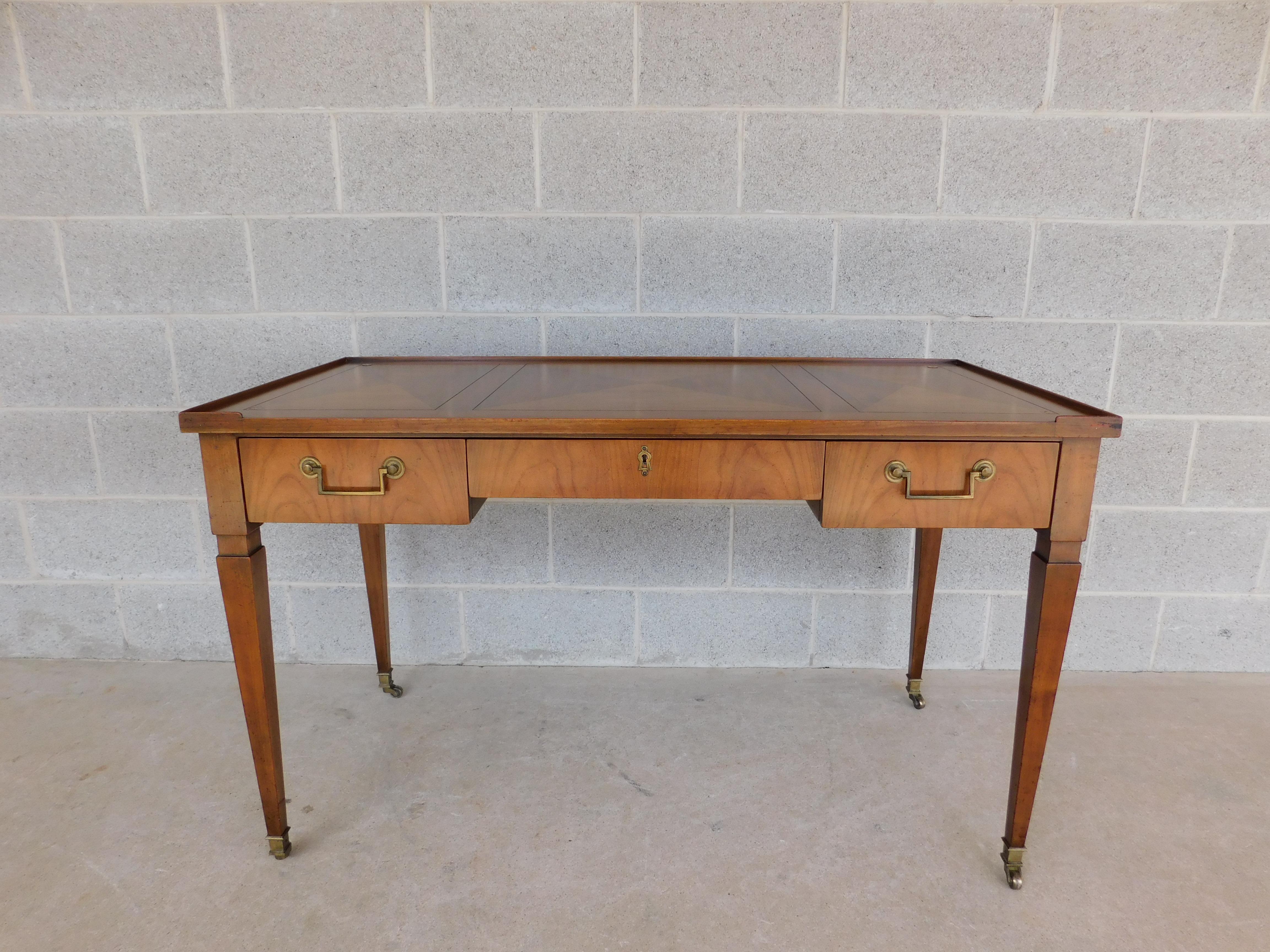 Midcentury Baker Furniture Regency style writing desk. Raised border edge surrounding the diamond pattern three part writing surface. 3 Dovetailed drawers, with brass pulls on the flanking left, and right drawers. Center locking drawer with original