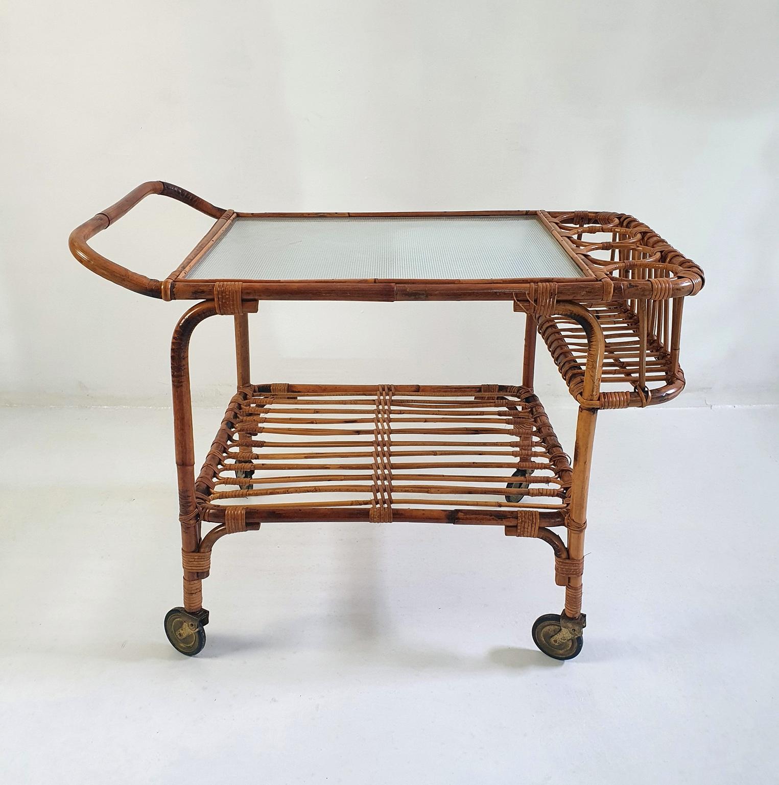 A rare rectangular Italian two tiered bar cart from the 1950's made from bamboo and rattan. The top is made from sturdy glass which is a benefit when mixing drinks. Can hold up to four bottles. Retains the original castors and has an overall nice