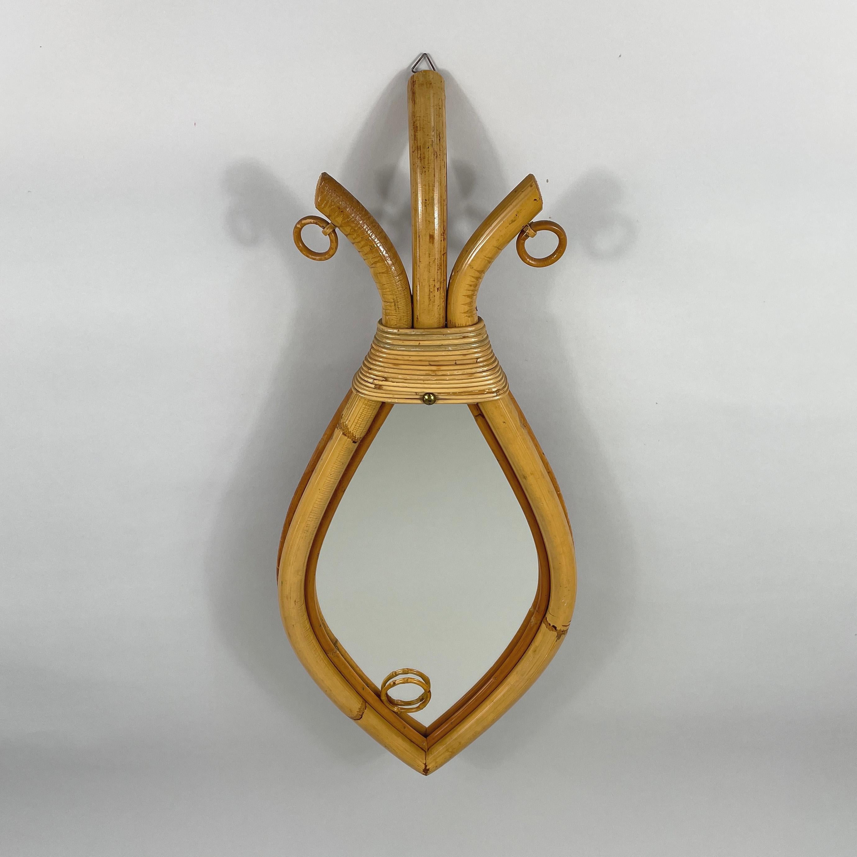 Questo insolito specchio artigianale, progettato in Francia negli anni '50, presenta un design unico e artistico. La cornice dello specchio è realizzata in bambù e rattan, a forma di pesce. La struttura è allungata, con la parte più larga che