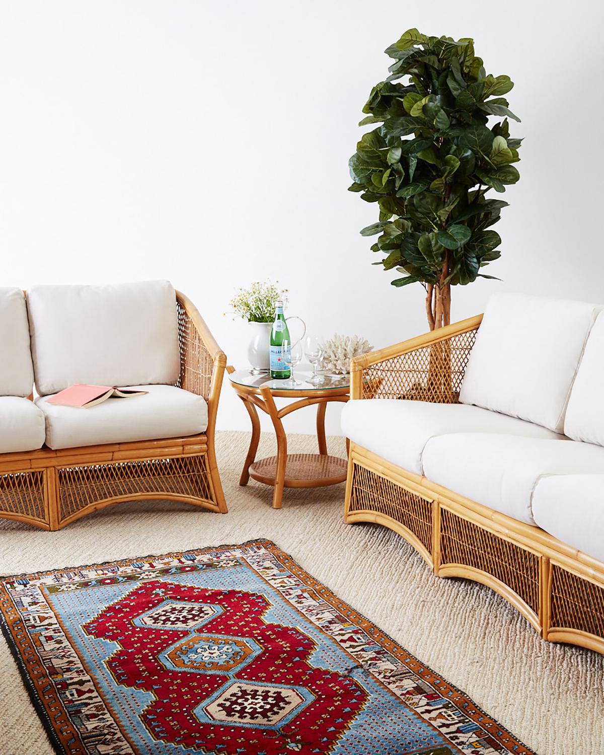 Sculptural Mid-Century Modern bamboo rattan and wicker settee or loveseat. Constructed from bent rattan with a waisted form and graceful curved arches. Decorated with geometric wicker design insets. Made in the Hollywood Regency taste with newly