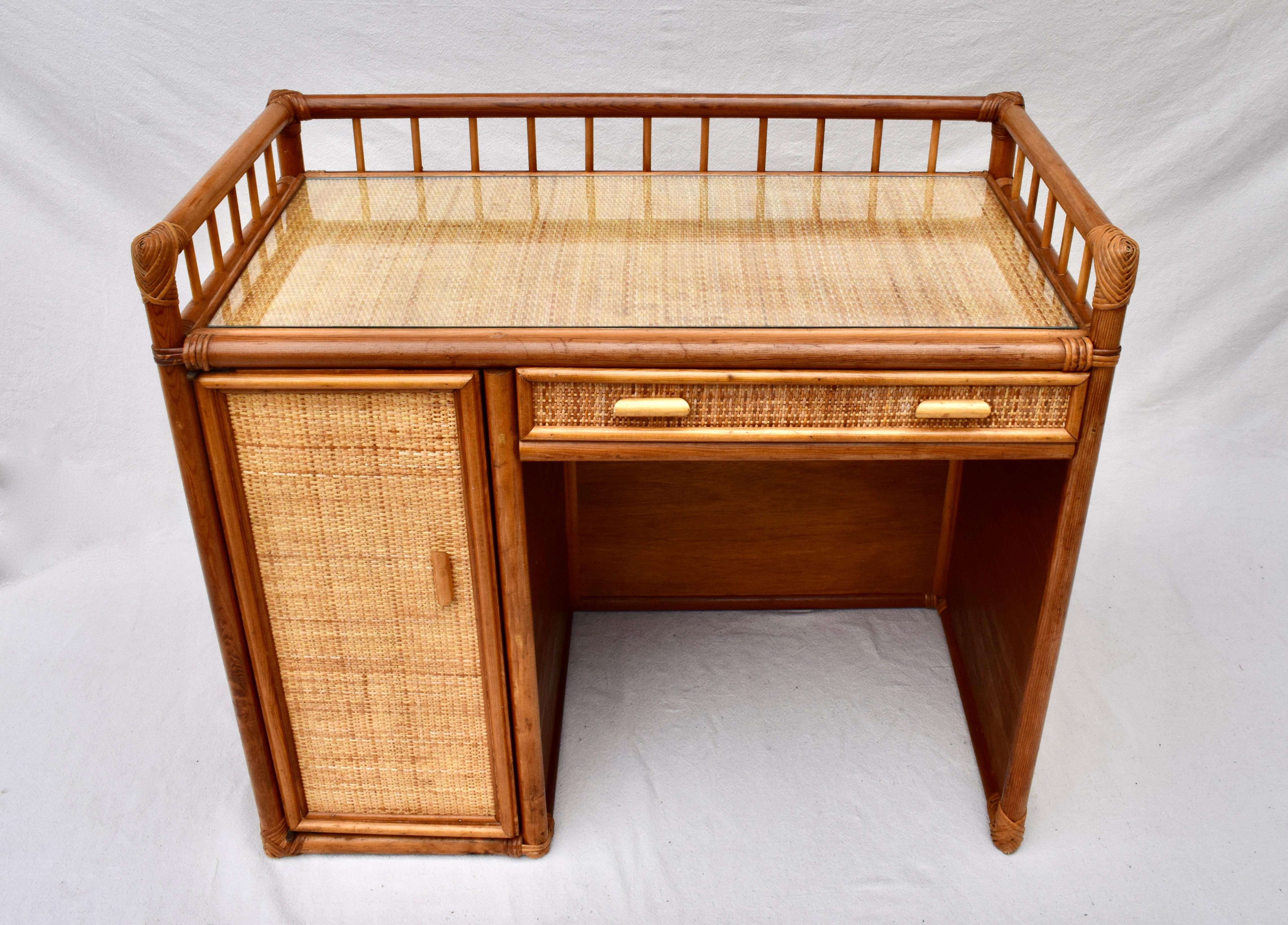 An unusual small scale bamboo rattan & grasscloth writing desk with single drawer, door & shelf. Interesting gallery detailing to the top; Includes custom glass top. 1970's made in Italy.