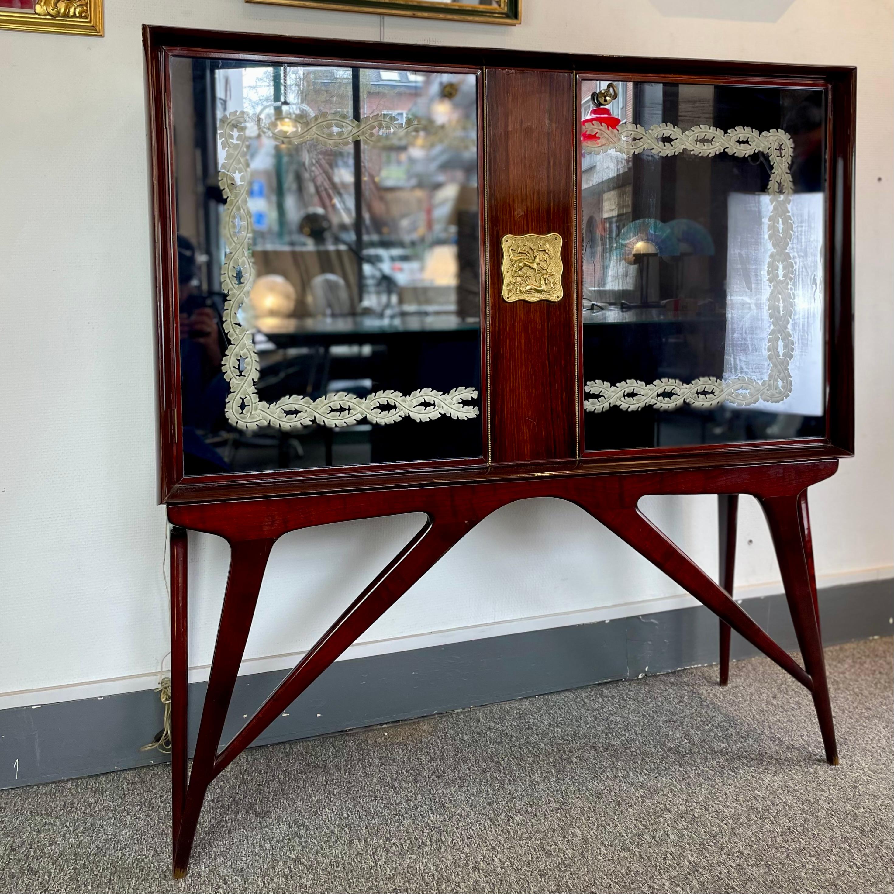 Espléndido mueble bar de mediados de siglo fabricado con maderas nobles, espejo de mercurio e incrustaciones de latón. En el interior, los cristales y espejos se subliman mediante un sistema de iluminación conectado a la apertura de las puertas.
