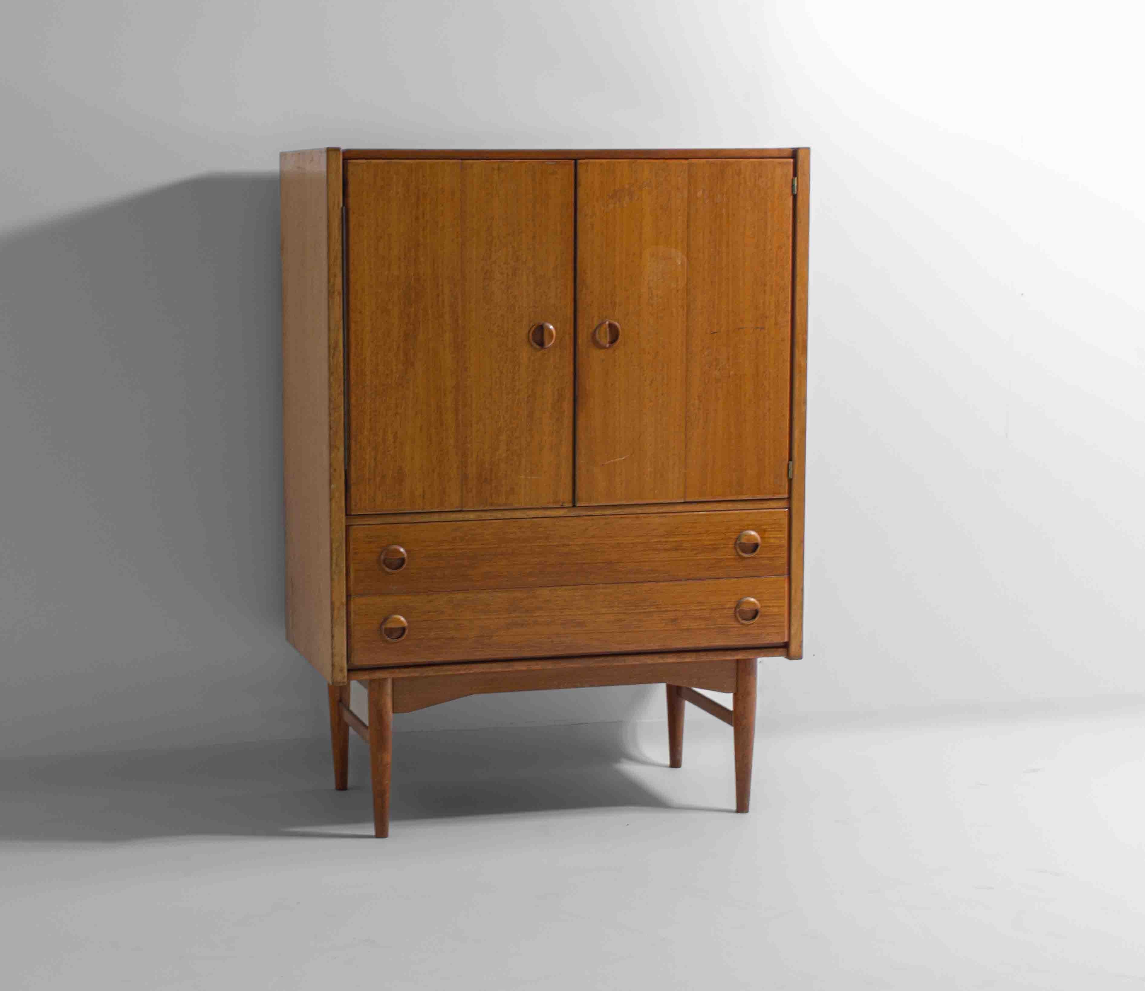 Mobile bar compatto e pulito degli anni '60. Realizzato in legno dai toni caldi, con maniglie rotonde integrate e ante pieghevoli che si aprono per rivelare un ampio spazio di archiviazione. Sotto ci sono due cassetti per gli occhiali, gli attrezzi