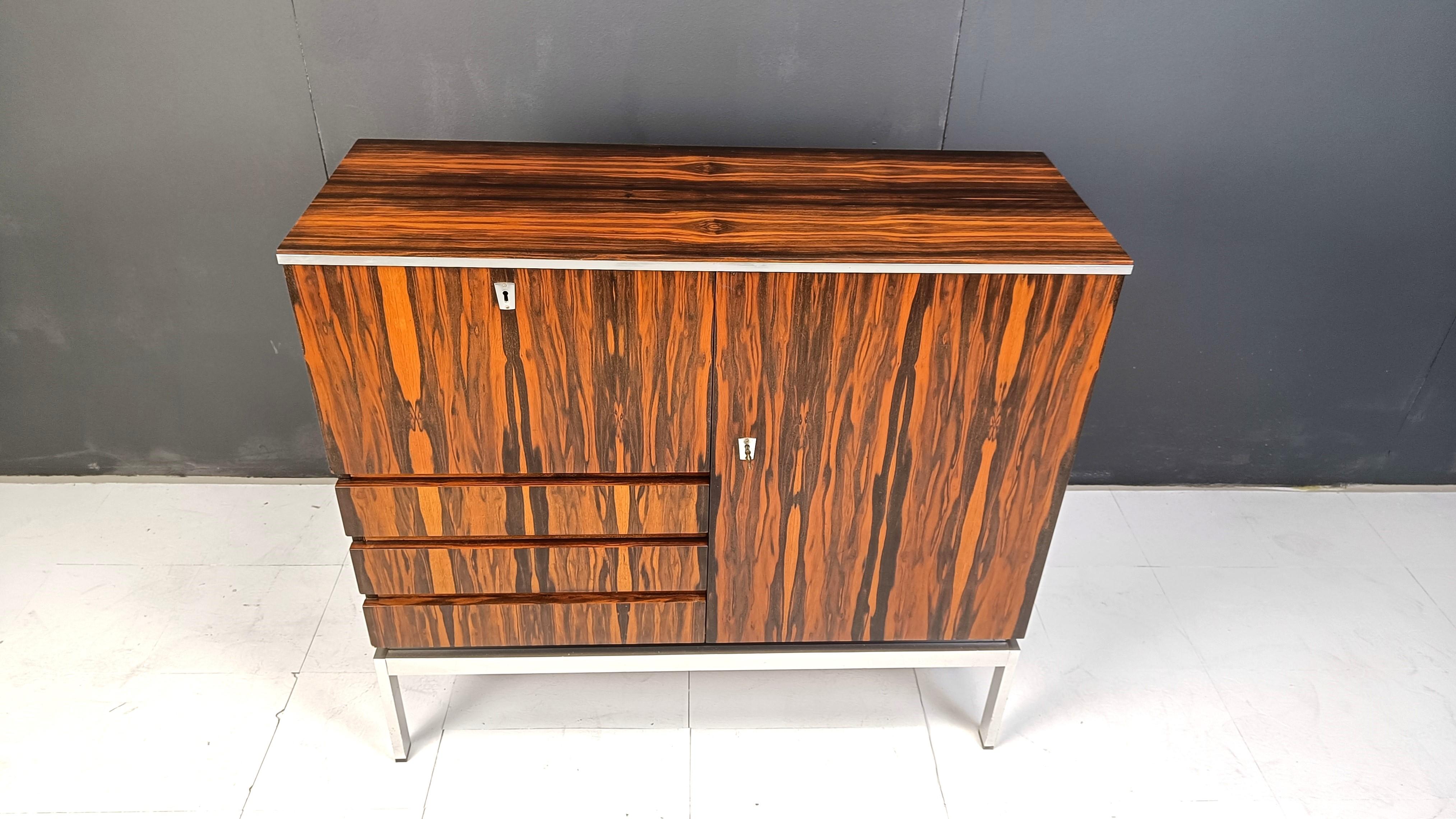 Wunderschöner Schrank aus exotischem Holz mit einer Tür, einer umklappbaren Platte, die eine verspiegelte  Barfach und drei Schubladen.

Verchromter Metallsockel.

Beachten Sie das fantastische Holzmuster.

1960er Jahre - Belgien

Guter