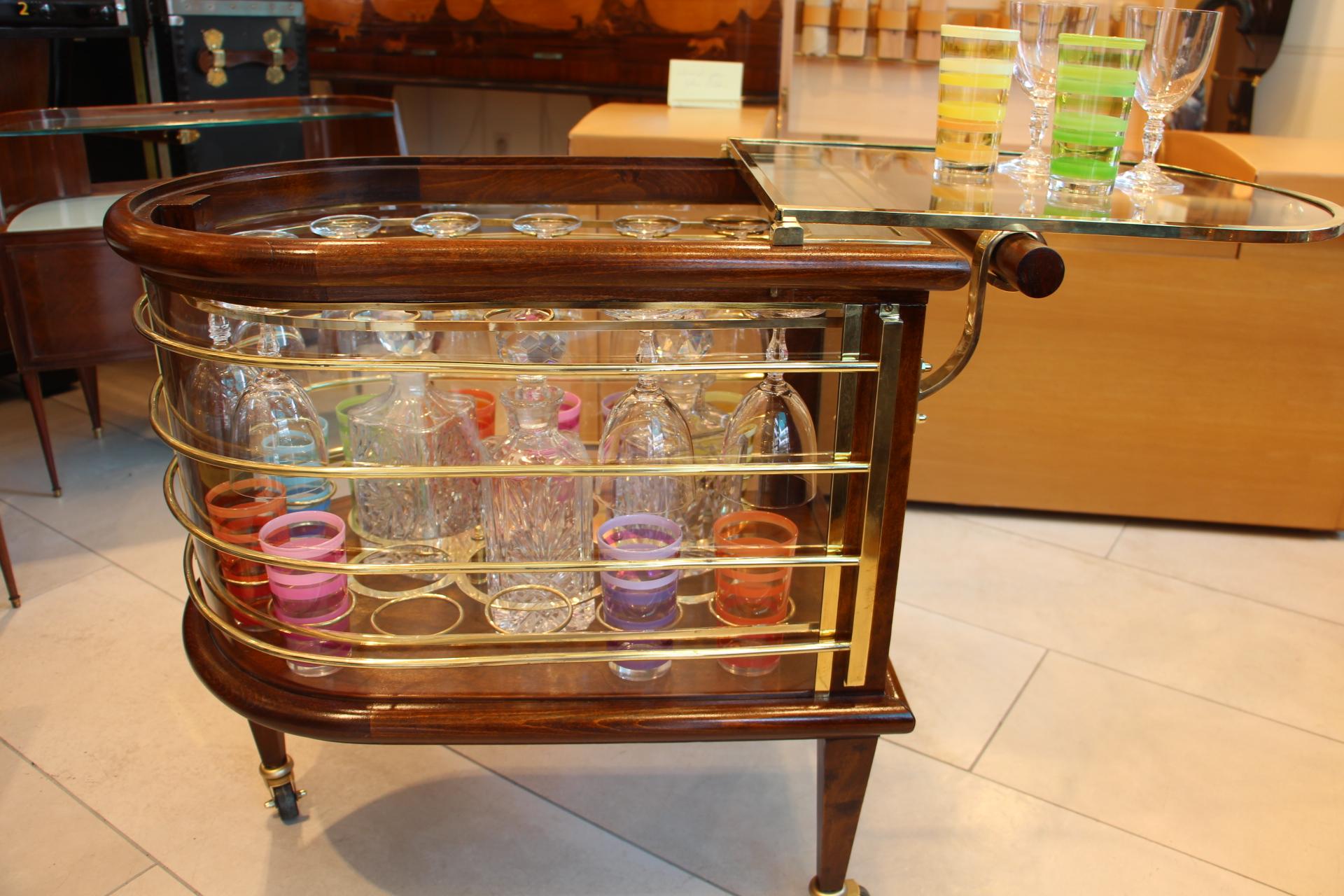 This fabulous bar cart from Louis Sognot features rounded sides with brass slats all around. Its general shape evokes a nautical accent. To open it and reach glasses and bottles, its glass top lifts and can be used to put glasses on. Inside is fully