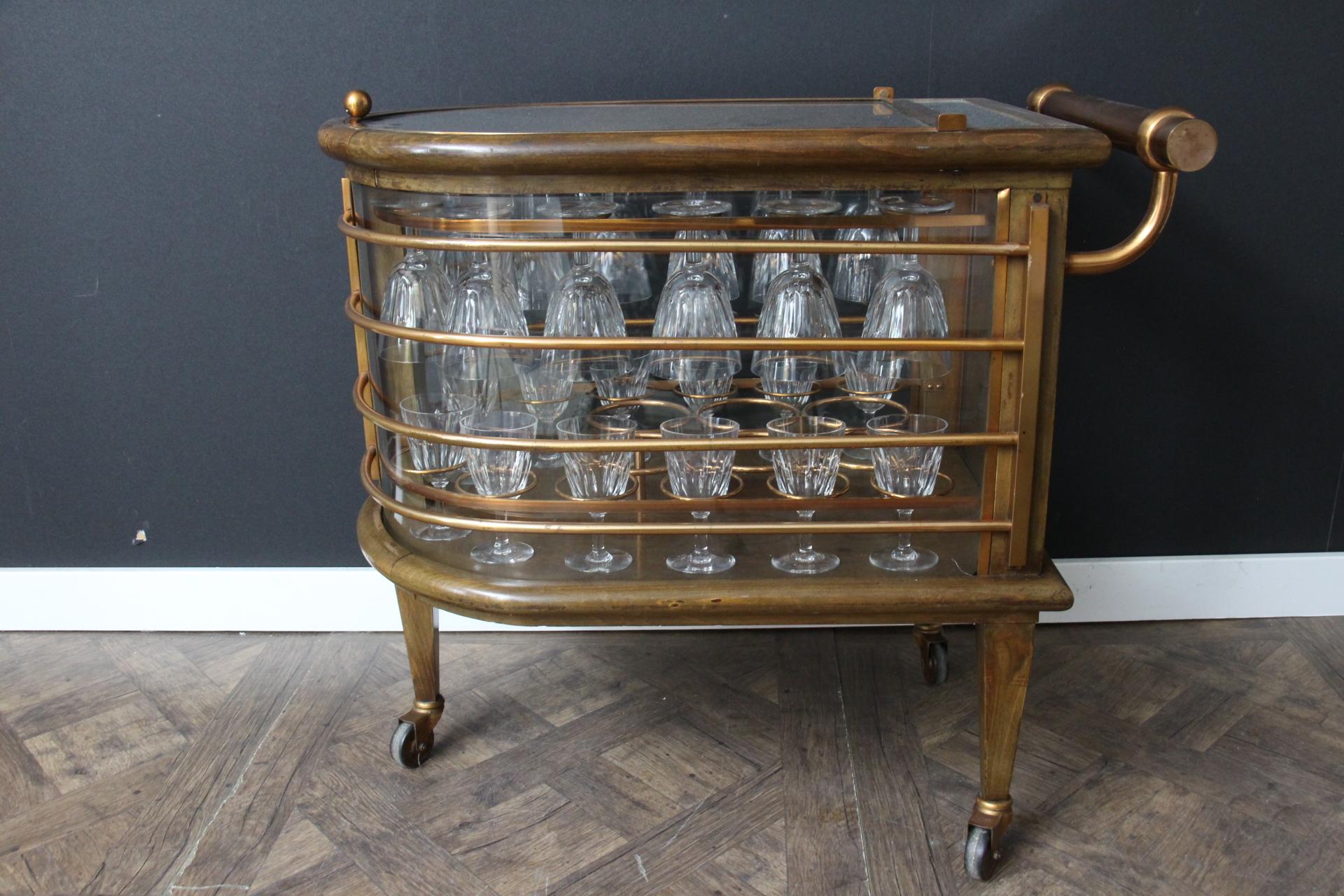 This fabulous bar cart from Louis Sognot features rounded sides with copper slats all around. Its general shape evokes a nautical accent. To open it and reach glasses and bottles, its glass top lifts and can be used to put glasses on. Inside is