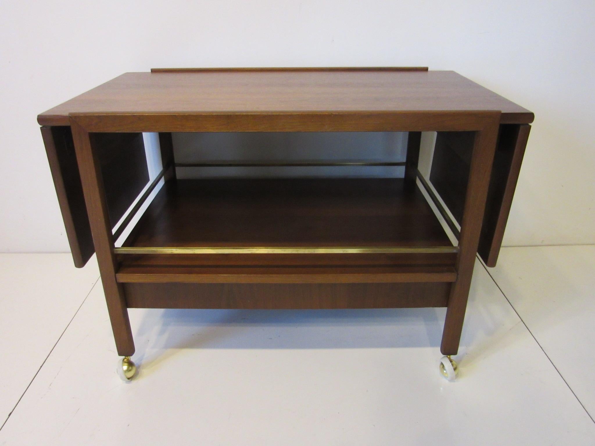 A medium toned walnut rolling bar / entertainment or TV cart with folding top and lower storage area with drawer. Detailed with brass rails and wheels this piece can be used in many ways, well crafted and well finished. Measurements when fully