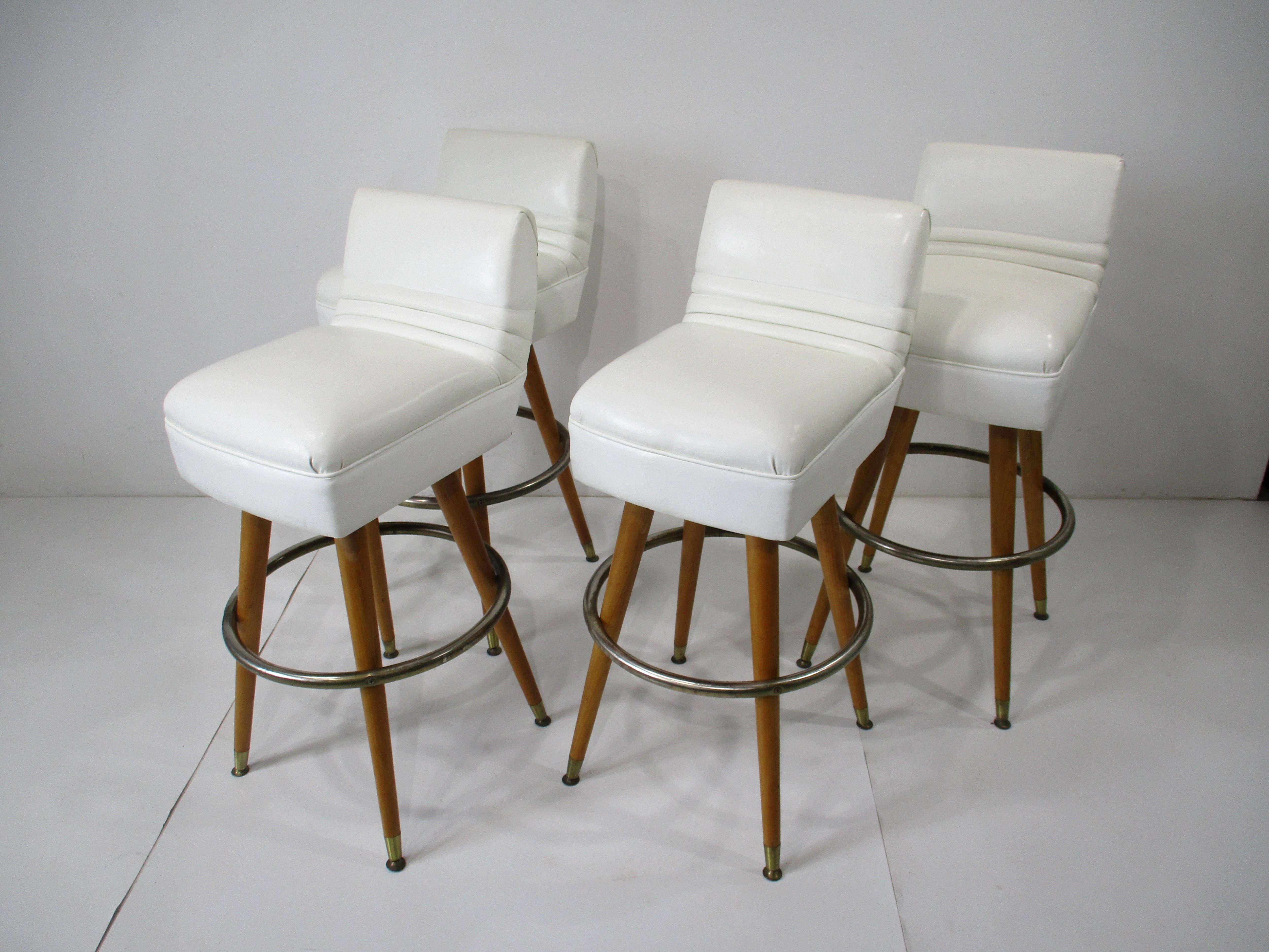 Un conjunto de taburetes de bar no giratorios con tapicería de polipiel blanca y bordes de respaldo con tachuelas de botones . Las patas cónicas de arce, a la manera del diseñador Paul McCobb, dan a estos taburetes de bar y mostrador ese aire de