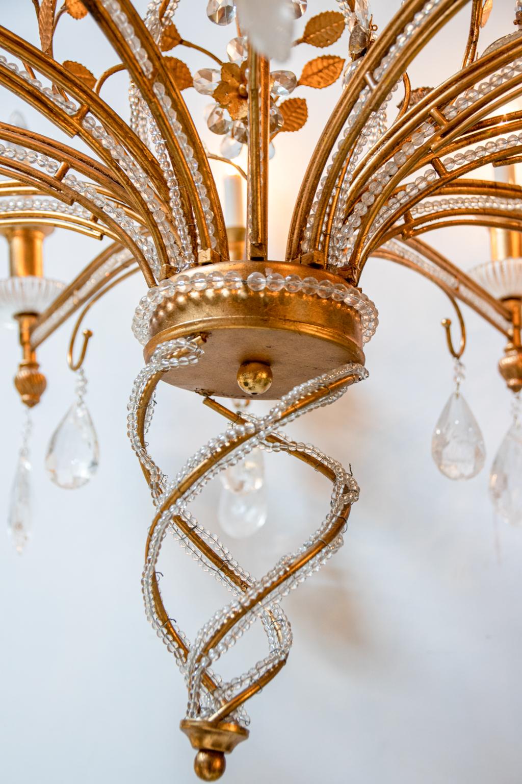 Circa mid-20th century Baroque style rock crystal chandelier with gilded metal, beaded strands accenting the arms, and foliage motifs. The piece is further decorated throughout with cut rock crystal prisms in the shape of pendant almonds along with
