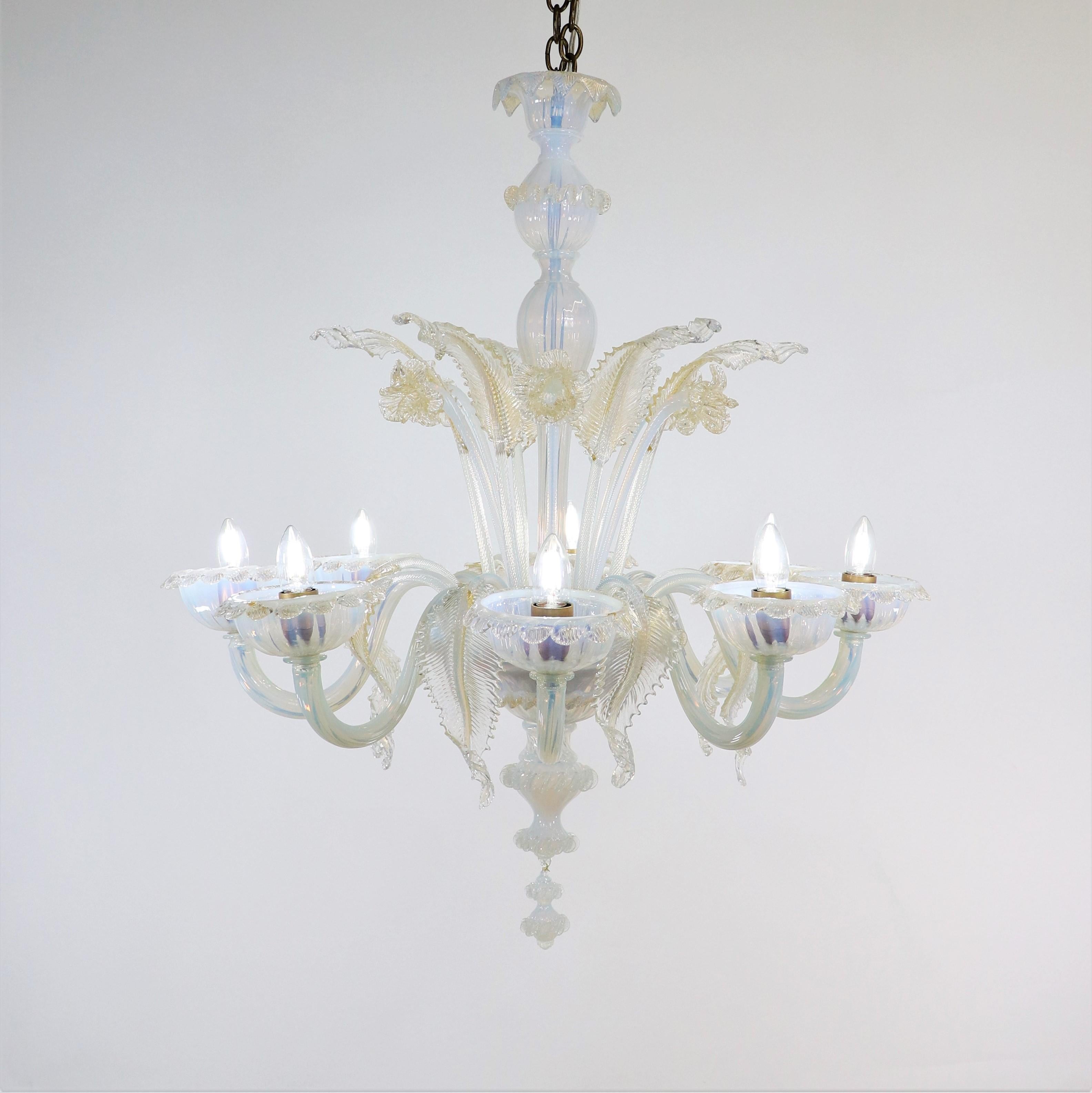 Questo lampadario opalino di Murano, squisitamente realizzato a mano, è dotato di otto bracci ondulati con coppe bordate di petali. Il vetro opalino lattiginoso vira verso un colore azzurro con sottili variazioni di luce. Narcisi e foglie