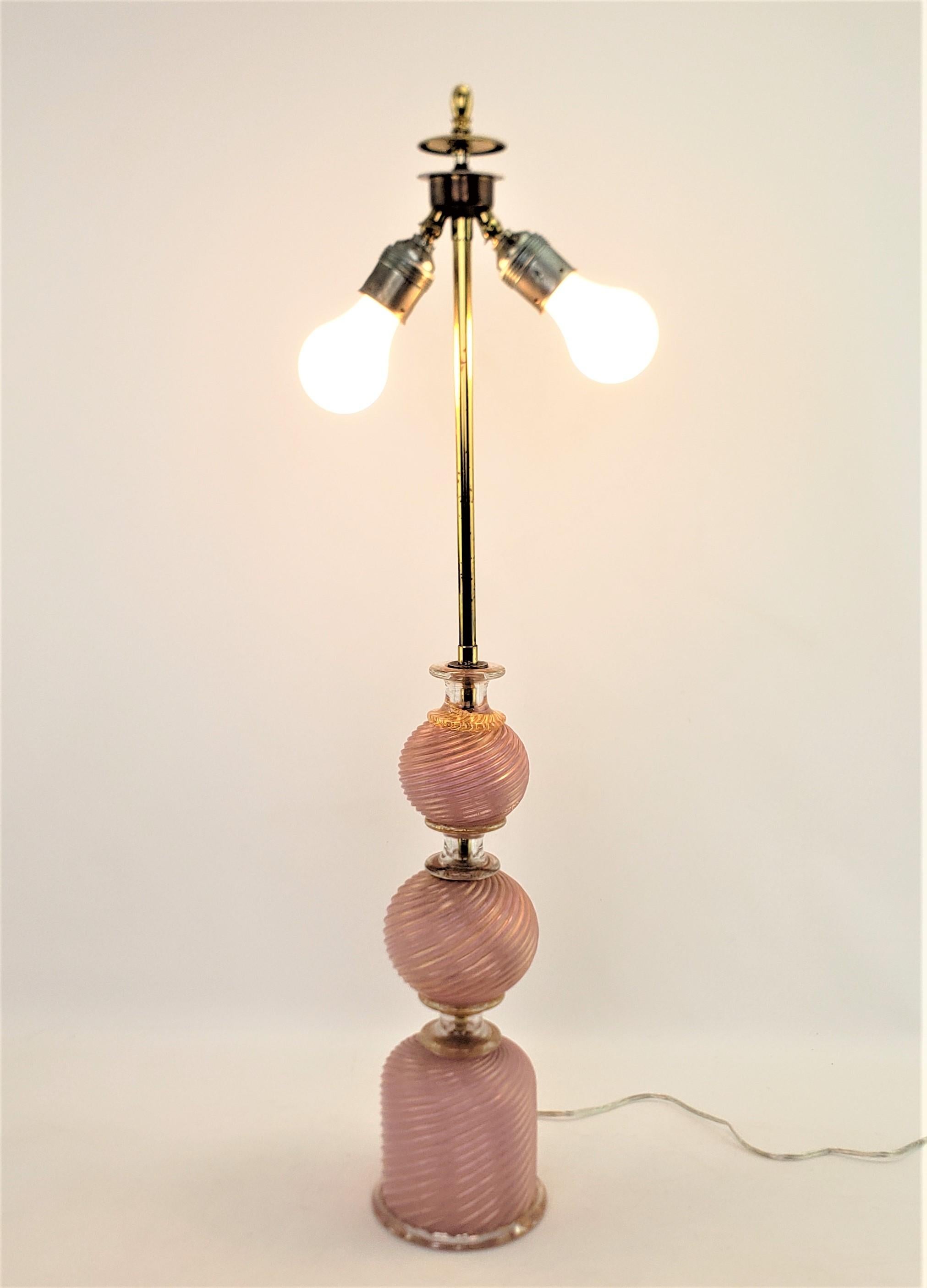 This Art Glass table lamp is unsigned, but presumed to have been done by the Barovier studio of Murano Italy in approximately 1965 and done in the period Mid-Century Modern style. This art glass table lamp is done with a swirled cranberry glass with