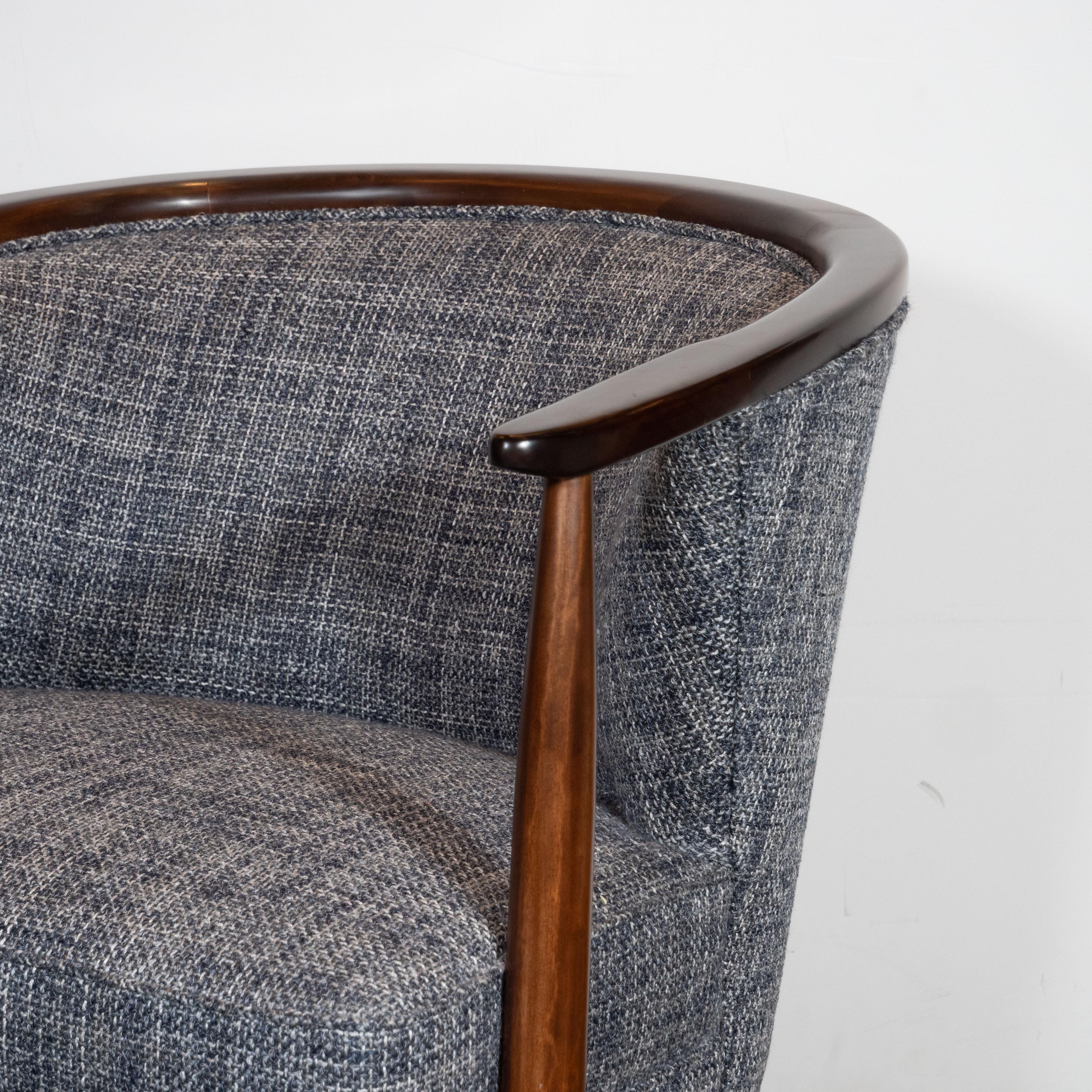 This elegant pair of Mid-Century Modern barrel back chairs were realized in the United States, circa 1950. They offer a dramatically curved back with handrubbed walnut detailing at the top that adjoins the cylindrical walnut arms that taper at each