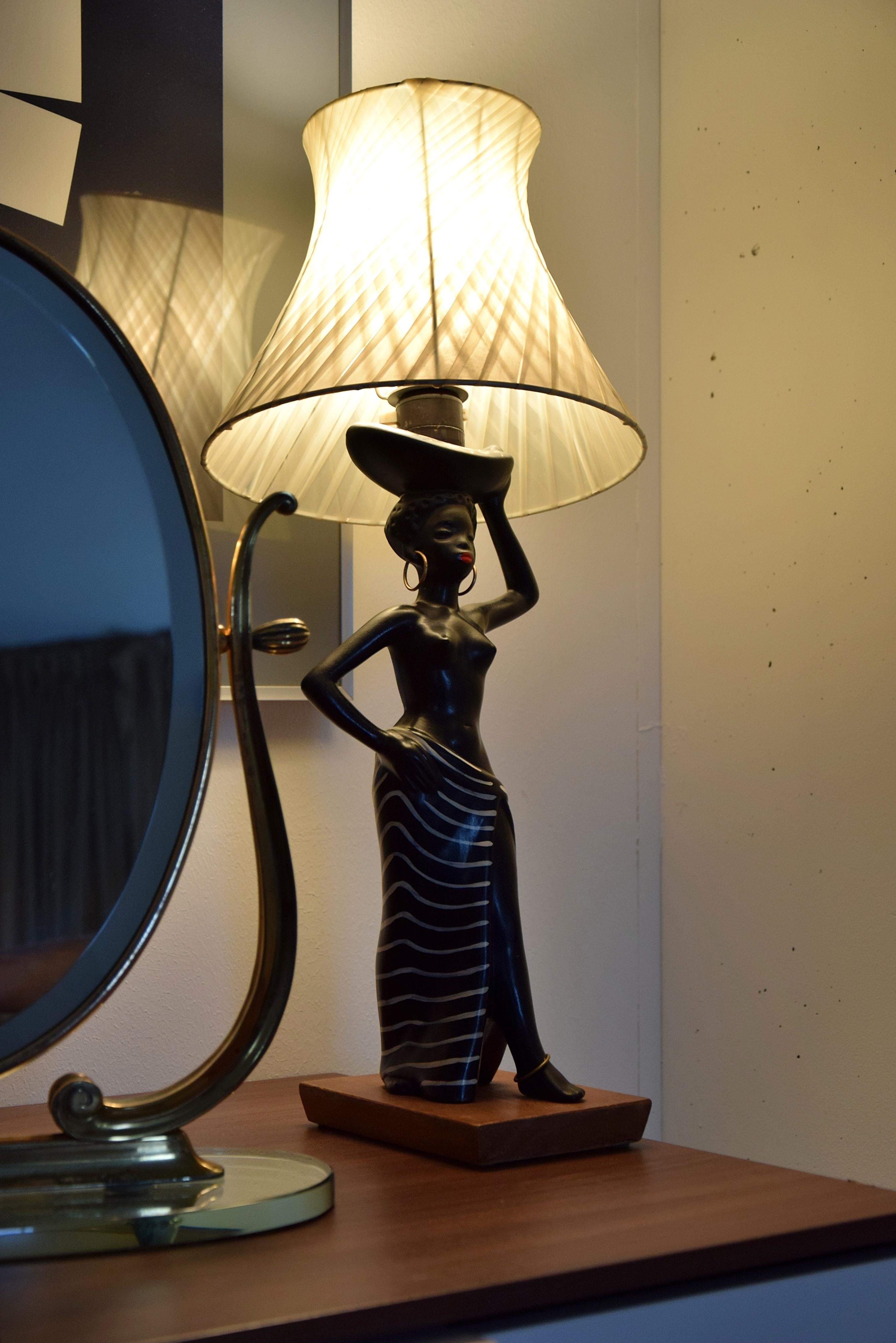 Lámpara de mesa Barsony de cerámica de color negro mate con figura femenina que lleva una cesta. Fabricado en Australia en la década de 1950.

Esta belleza se enviará asegurada al extranjero en una caja de madera hecha a medida. El coste del