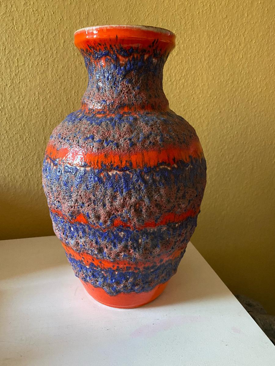 Eine atemberaubende und seltene Bay Keramik Bodenvase. Diese große Vase ist mit vulkanischen und dicken Lavaglasuren verziert. Der Korpus der Vase weist strukturierte vulkanische Glasuren in Blau und leuchtendem Orange auf, die Bänder bilden.
BAY