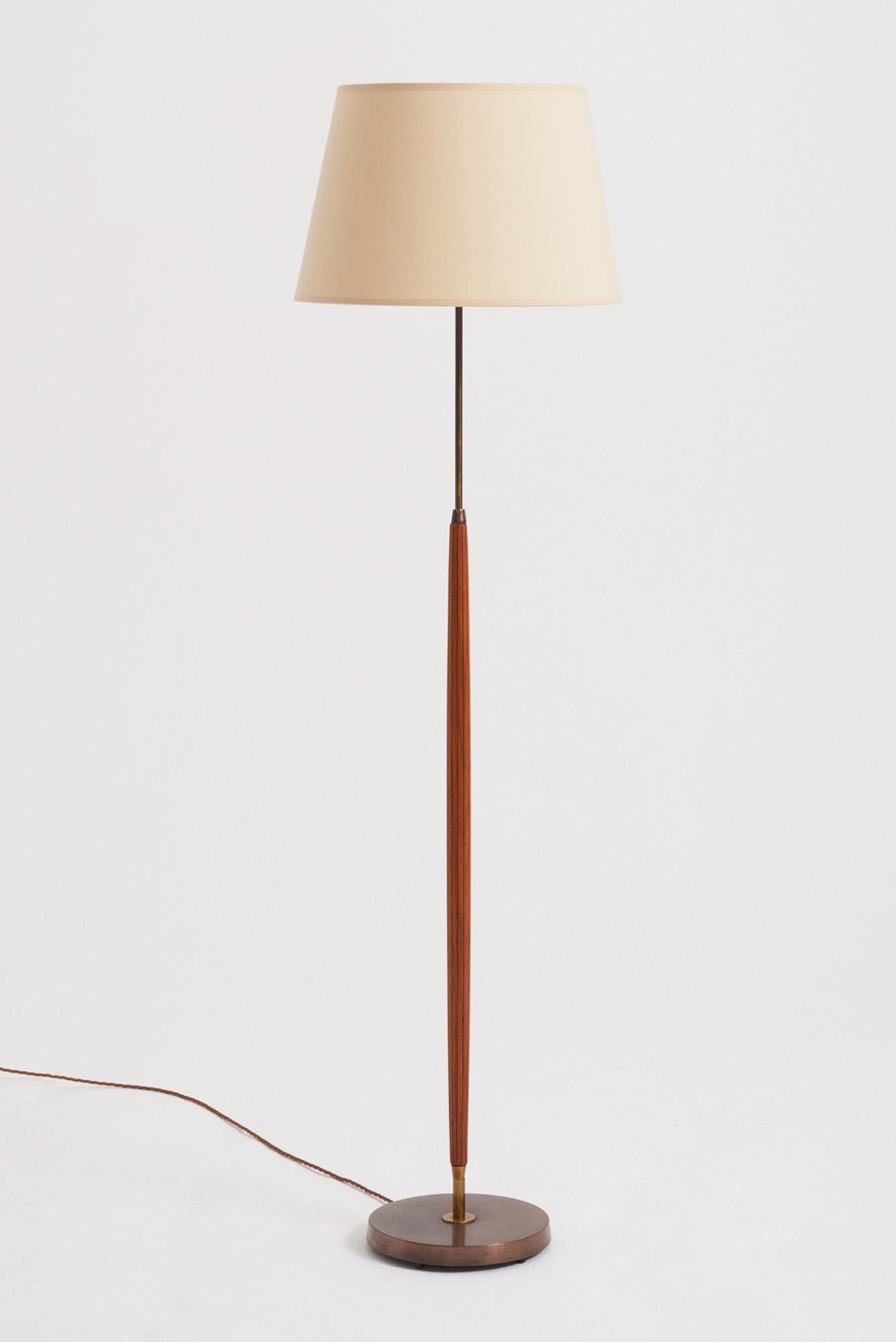 A brass and beech floor lamp by Falkenbergs Belysning. 
Sweden, third quarter of the 20th Century
With the shade: 153 cm high by 46 cm diameter
Lamp base only: 127 cm high by 24 cm diameter