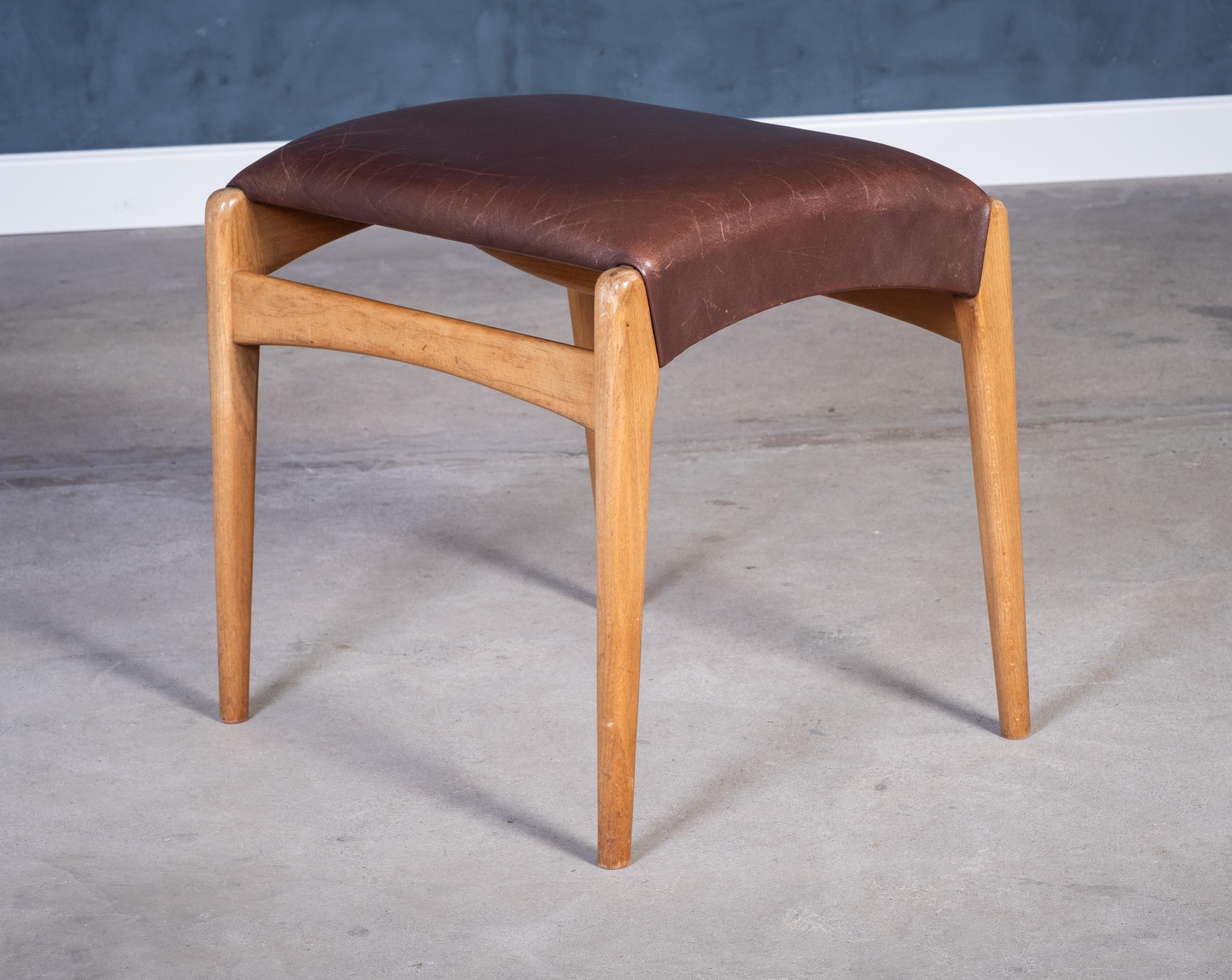 Charming mid-century stool crafted in beech wood with original brown leather upholstery. Produced by a Danish furniture maker around the 1950s, this piece reflects the clean lines and functional elegance typical of Scandinavian design from the