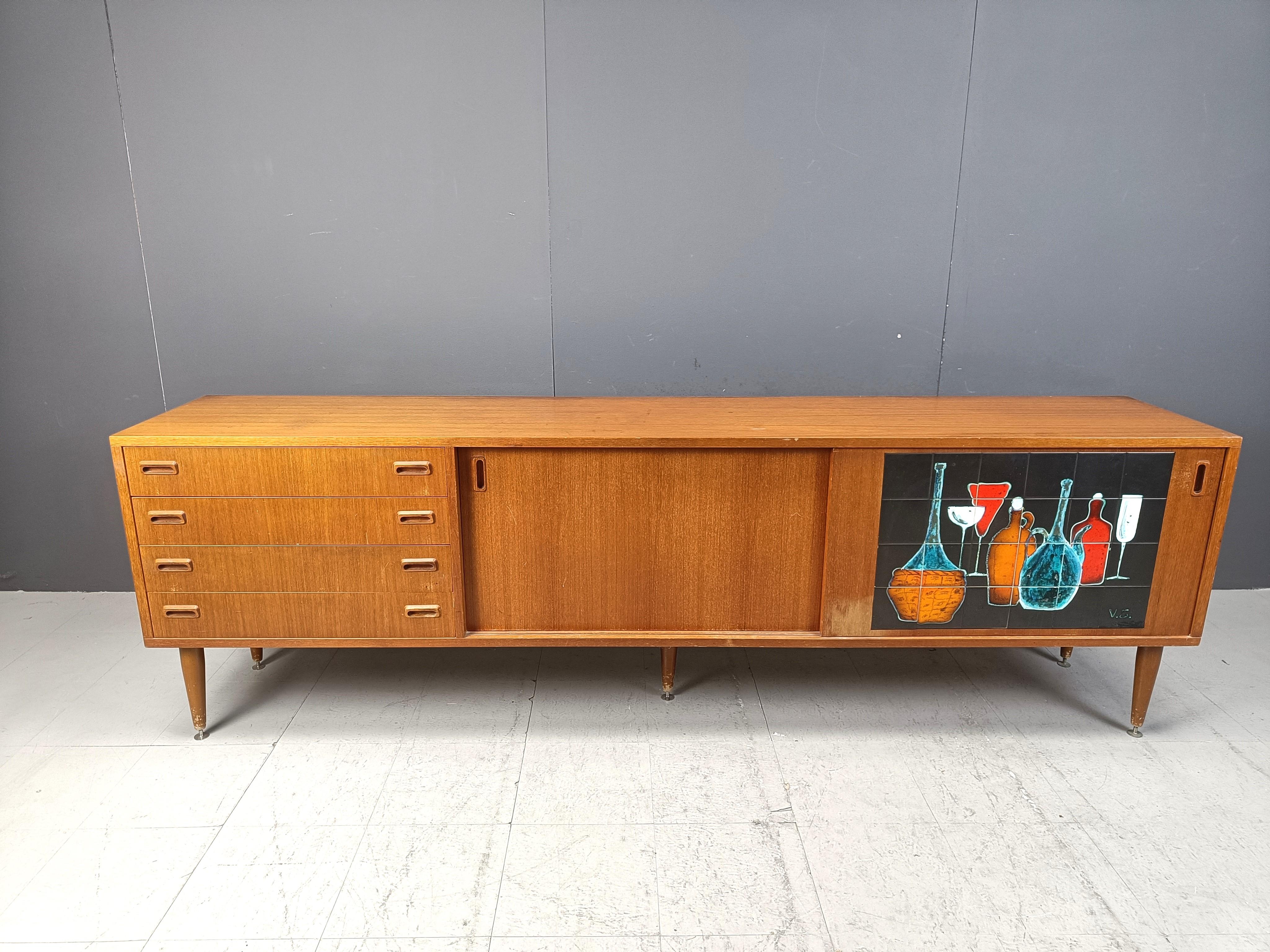 Credenza in teak di metà secolo con 2 porte scorrevoli e 4 cassetti

Opera d'arte in ceramica intarsiata (firmata) su una delle porte scorrevoli.

Anni '60 - Belgio

Condizioni generali buone

Dimensioni:

Altezza: 78 cm
Larghezza: 248