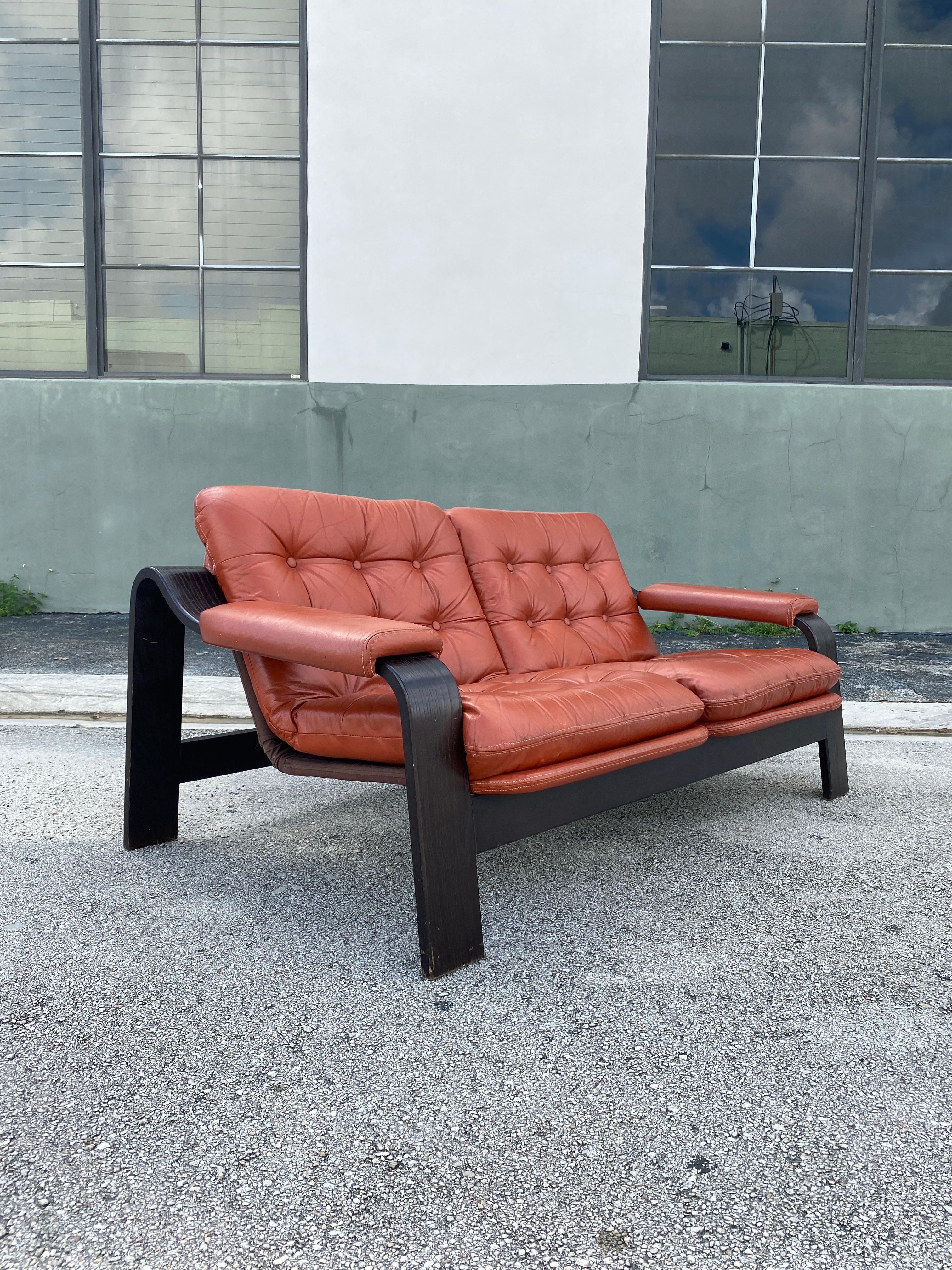Vintage lounge chair with original burnt orange leather sitting over brown canvas slings, bentwood frame finished in black walnut stain. Circa 1970s.

Measures: 57”W x 36”D x 25”H x 14”seat H x 19”arm H