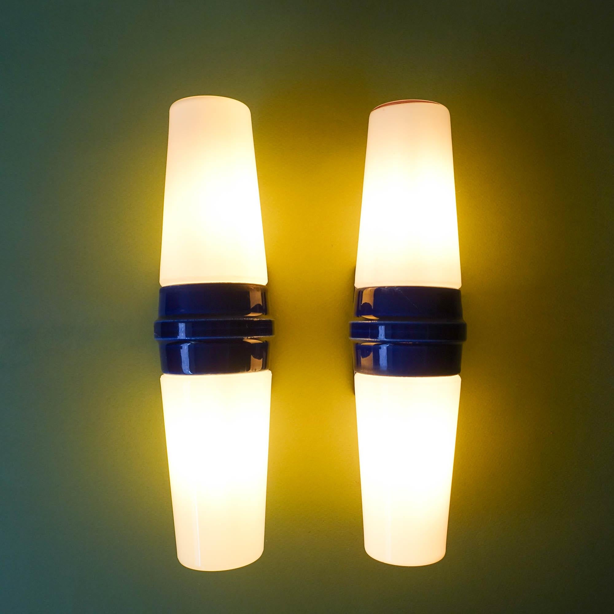 This pair of sconces, model 6060, from Bernadotte range, was designed by Sigvard Bernadotte for IFÖ, in Sweden, during the 1960's. Each one features a central piece in cobalt blue ceramic, that is fixed in the wall, and, in each side a white opaline