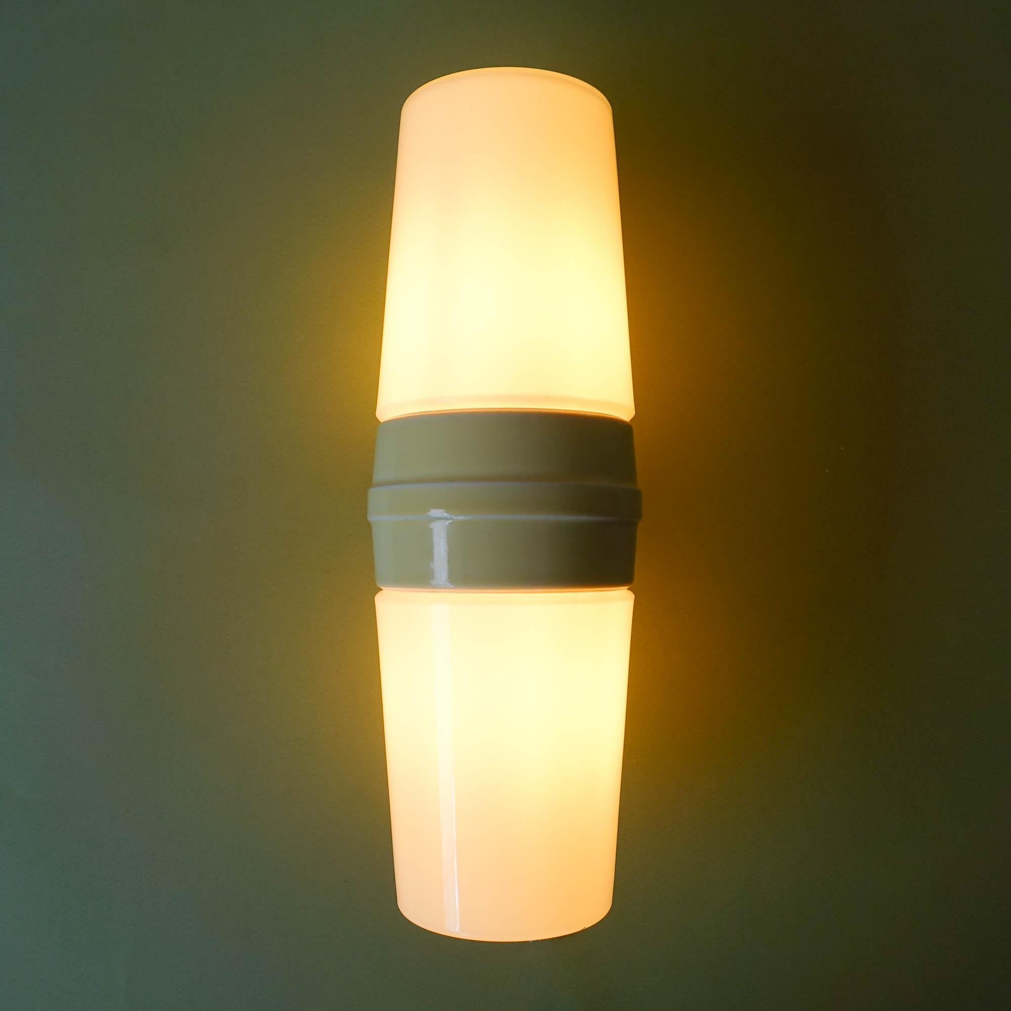 This sconce, model 6065, from Bernadotte range, was designed by Sigvard Bernadotte for IFÖ, in Sweden, during the 1960's. It features a central piece in light yellow ceramic, that is fixed in the wall, and, in each side a white opaline glass, that