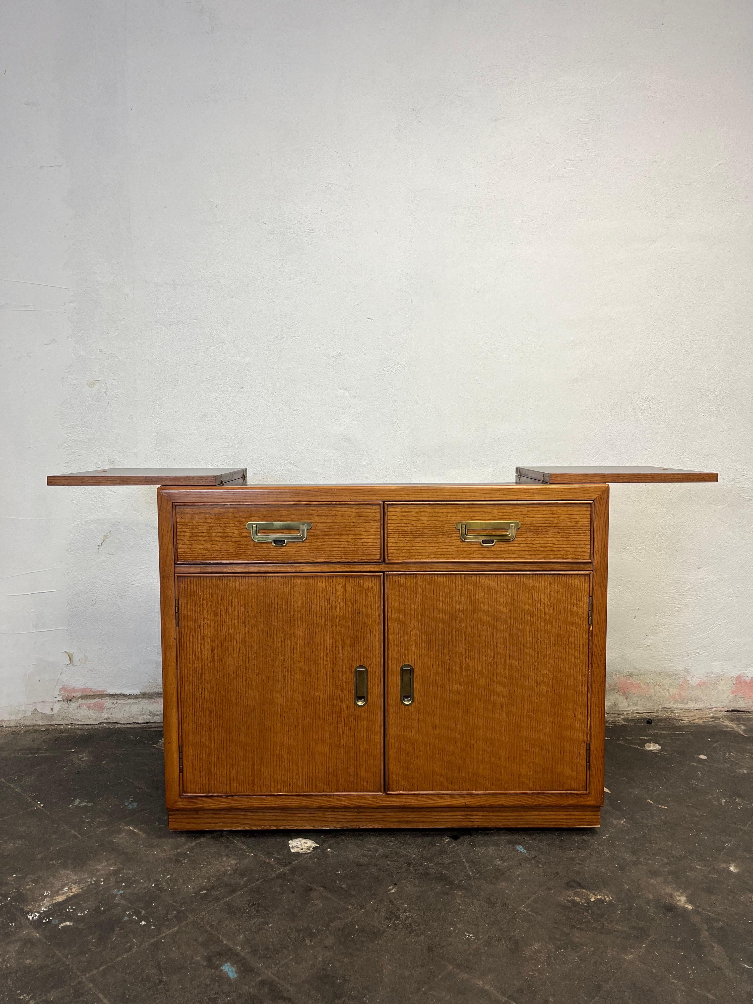 Vintage Bernhardt Campaign Flip Top Server. Classic campaign styling with brass fittings. Ample storage with 2 drawers, 2 doors open for open shelved interior. Top opens with brass ring pulls to expose laminate surface for hot or wet. 
Curbside to
