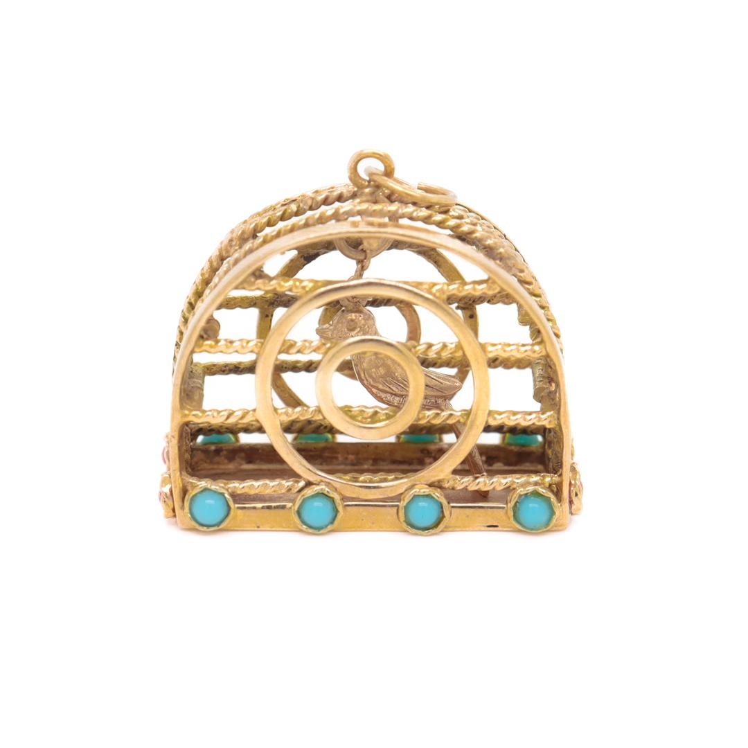 A fine figural bird cage charm.

In 14k gold.

In the form of a domed birdcage.

The interior set with a moving bird figurine that is suspended from the chain.

With turquoise cabochons set around the base.

Set with a bail to the top that allows