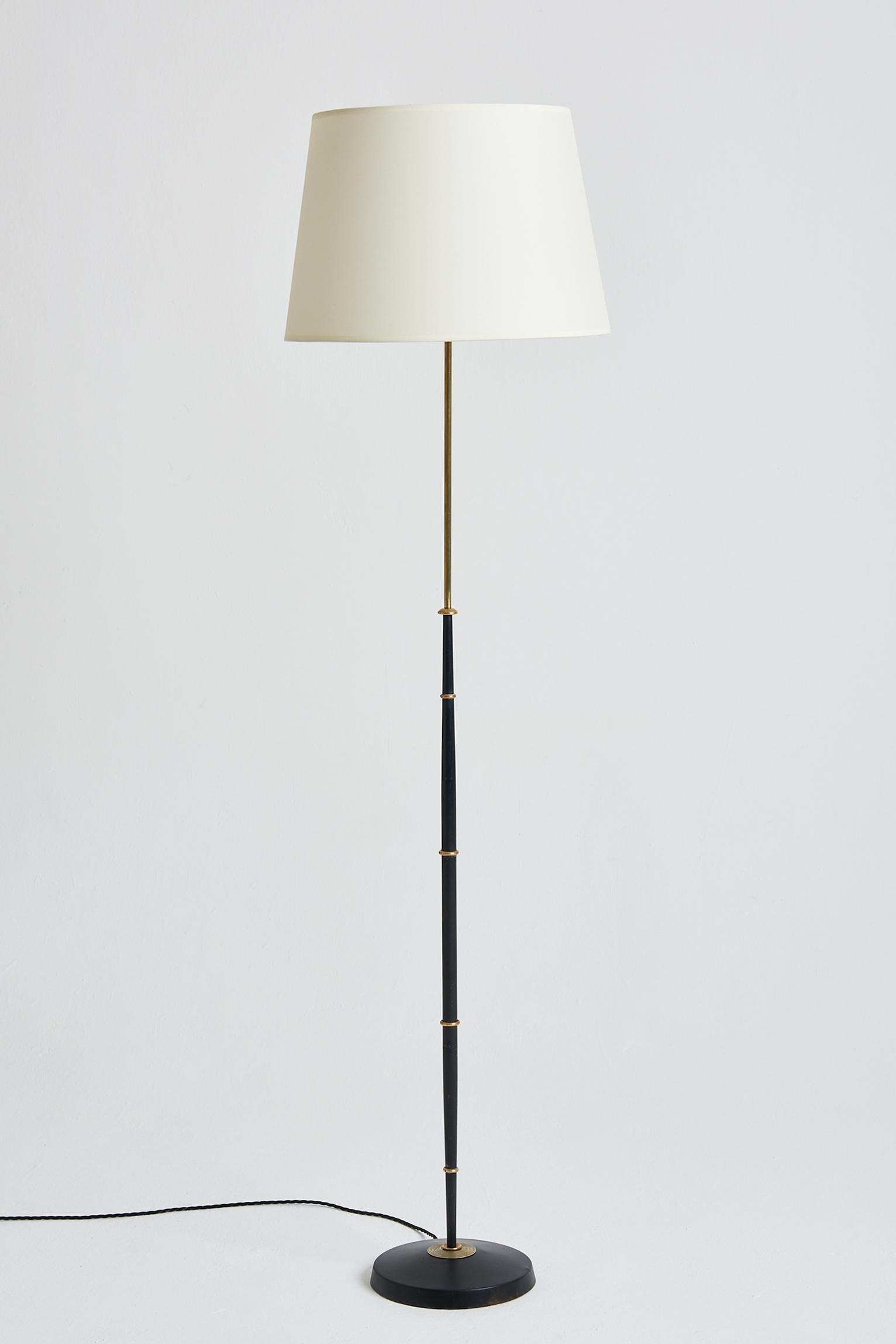 A brass and black enamelled iron floor lamp.
France, third quarter of the 20th Century. 
With the shade: 165 cm high by 41 cm diameter.
Lamp base only: 145 cm high by 25 cm diameter.