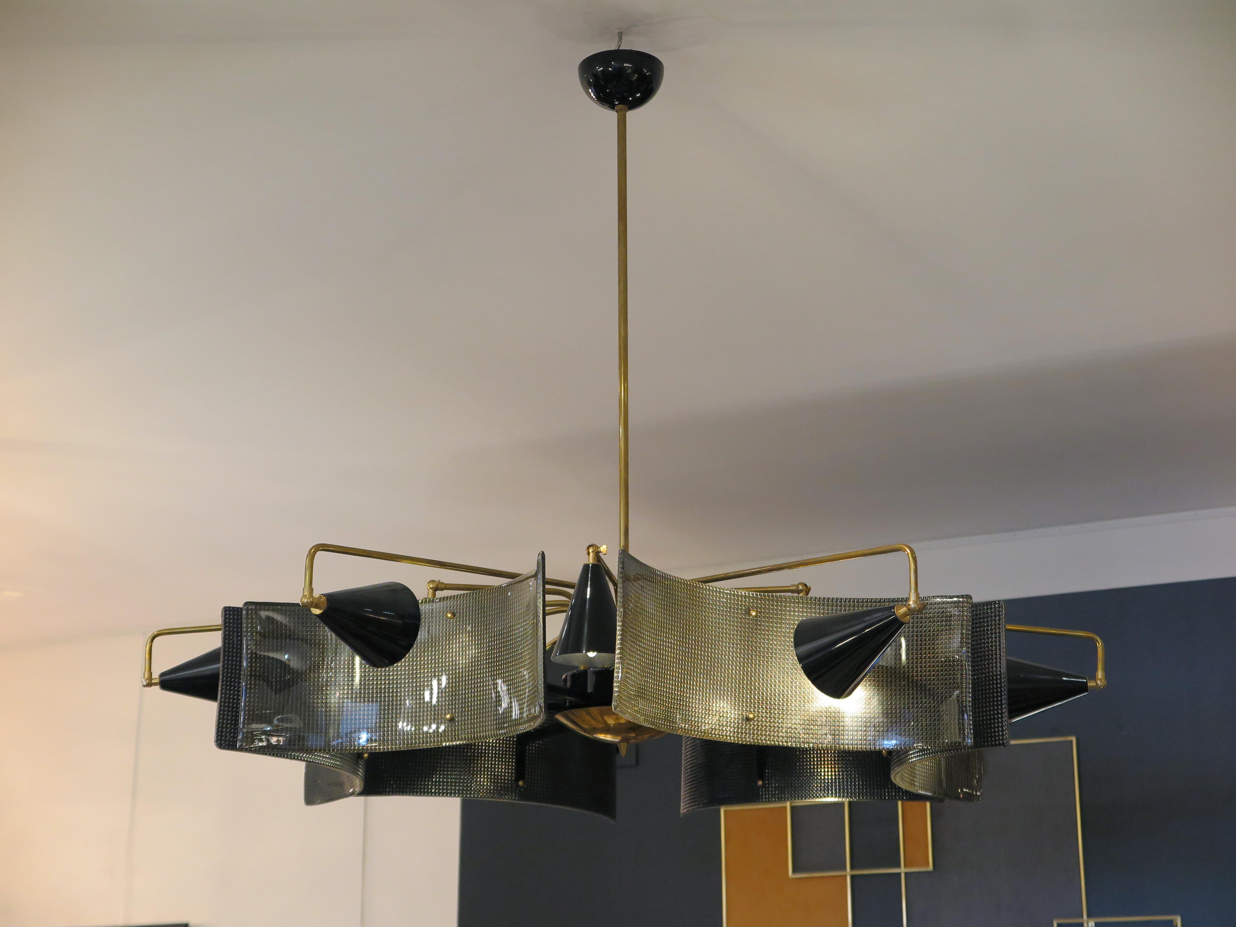 An edgy Mid-Century modern chandelier with curved and textured Murano glass panels. Black lacquer cone shades house the 12 bulbs surrounding the chandelier. Black lacquer arms support the Murano panels while brass arms support the lacquer shades. 

