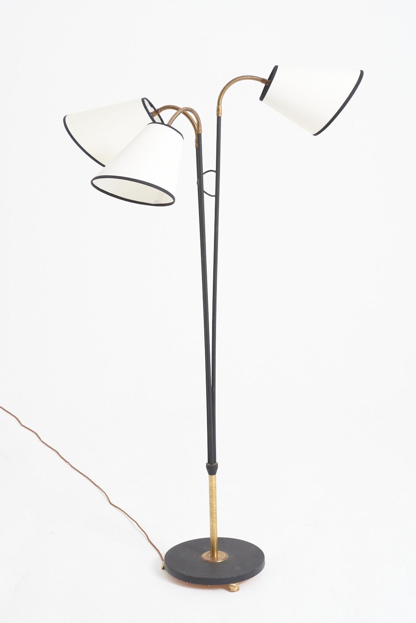 A brass and black enamelled iron three-arm floor lamp 
Sweden, 1950s
With the shade: 172 cm high by 77 cm diameter 
Lamp base only: 155 cm high by 50 cm diameter