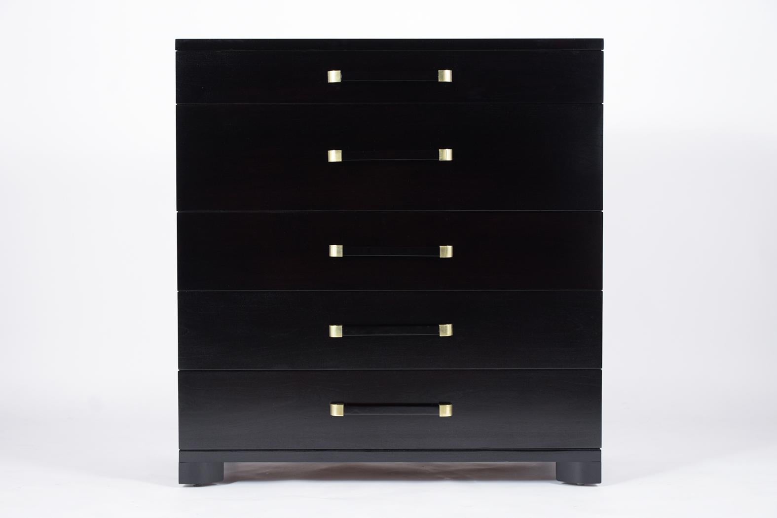 This Mid-Century Modern dresser for John Widdicomb Company is made of walnut wood, has a sleek design, and incredible ebonized lacquered finish. The dresser features 5 vertical drawers that each come with a large center carved wood handle with brass