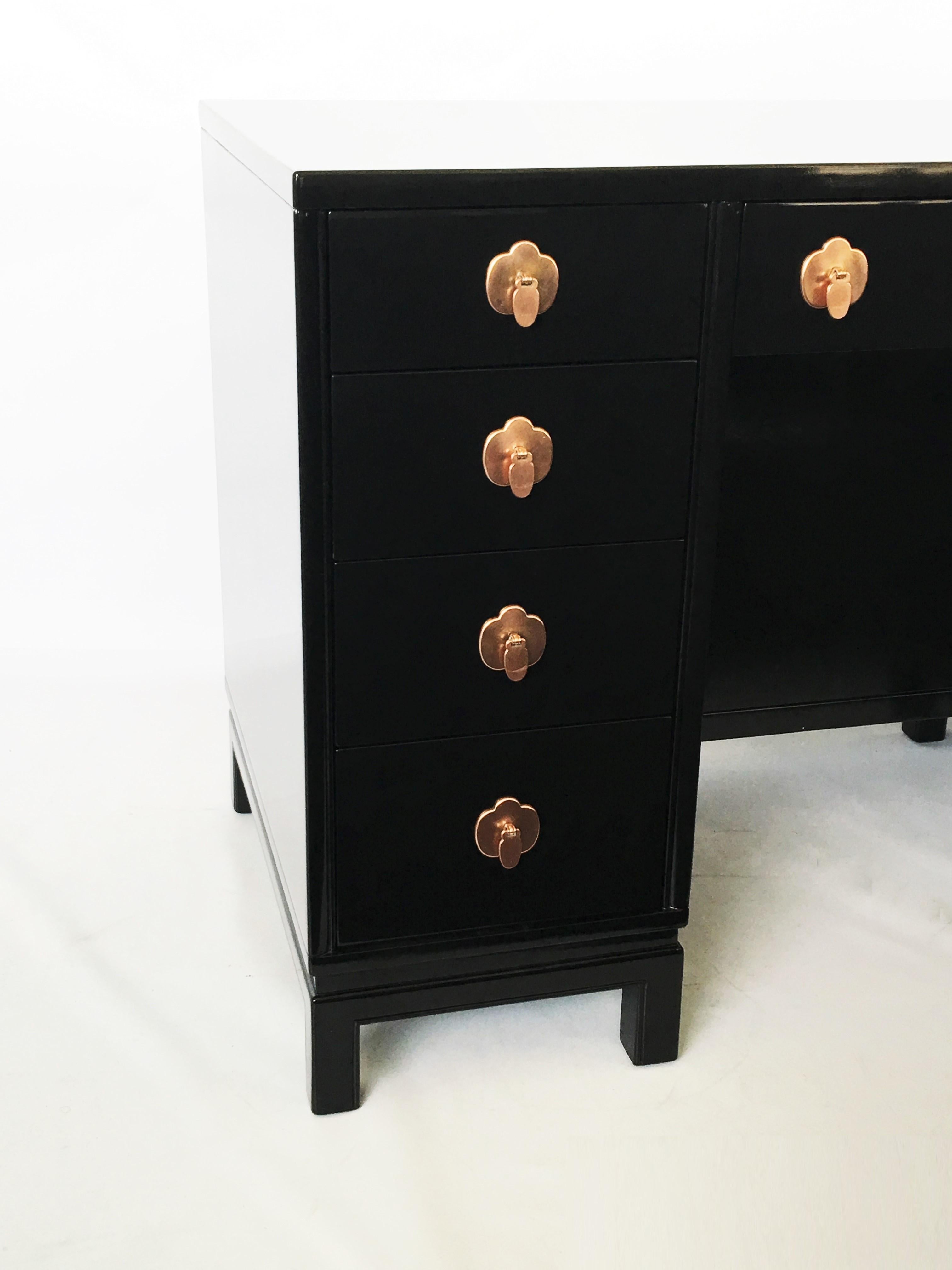 Asian style eight-drawer desk manufactured by Landstrom Furniture of Rockford, Illinois. Perfectly proportioned desk in black lacquer finish, chinoiserie styling with aged copper drop disc pulls and trefoil escutcheons on platform style four leg
