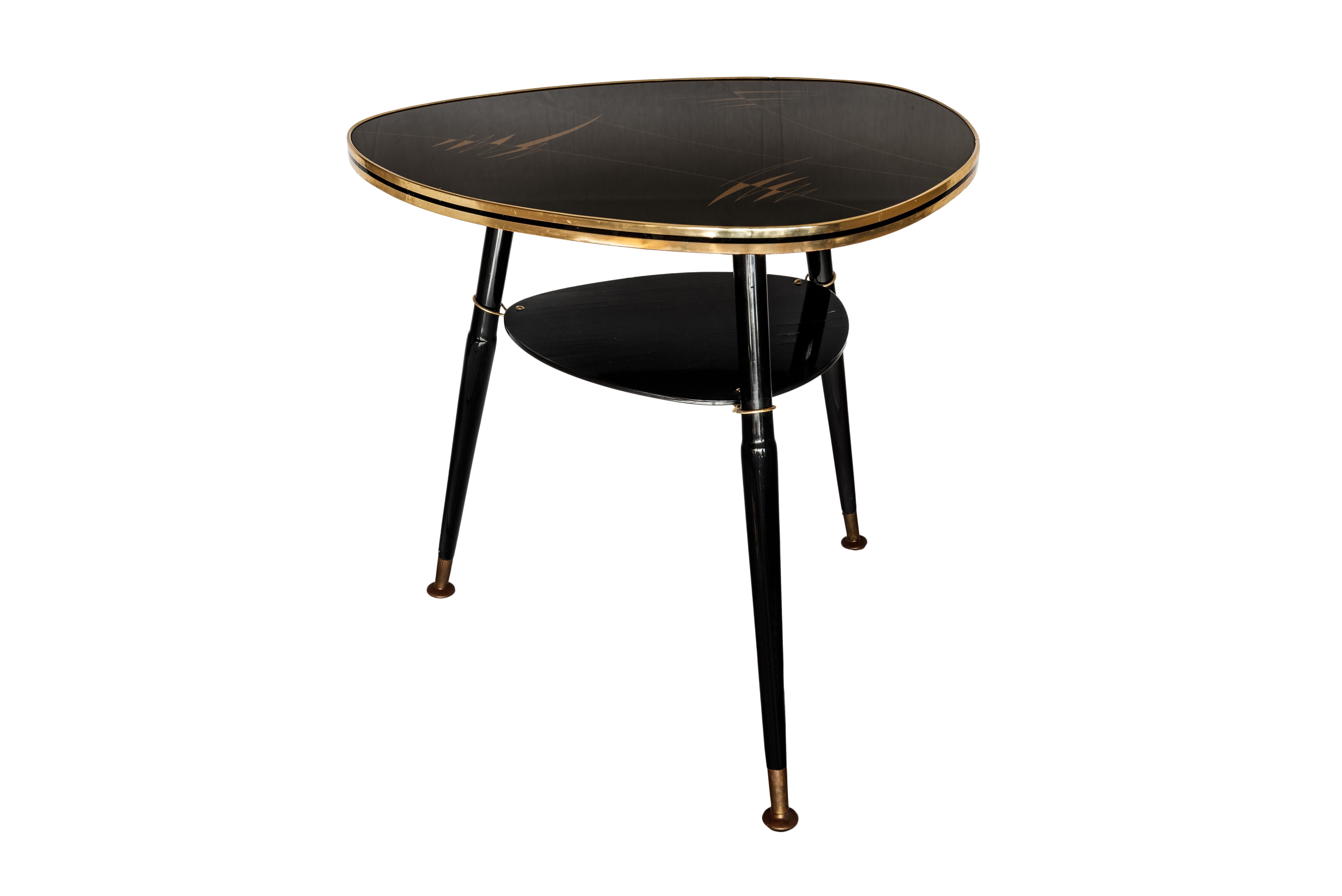 Midcentury black lacquered wood and Resopal glass plate, Ilse Möbel, Germany.
Midcentury coffee or side table from with a black glass Resopal tabletop with golden designs. Legs in wood and brass, with a lower plate under the main plate.
Produced