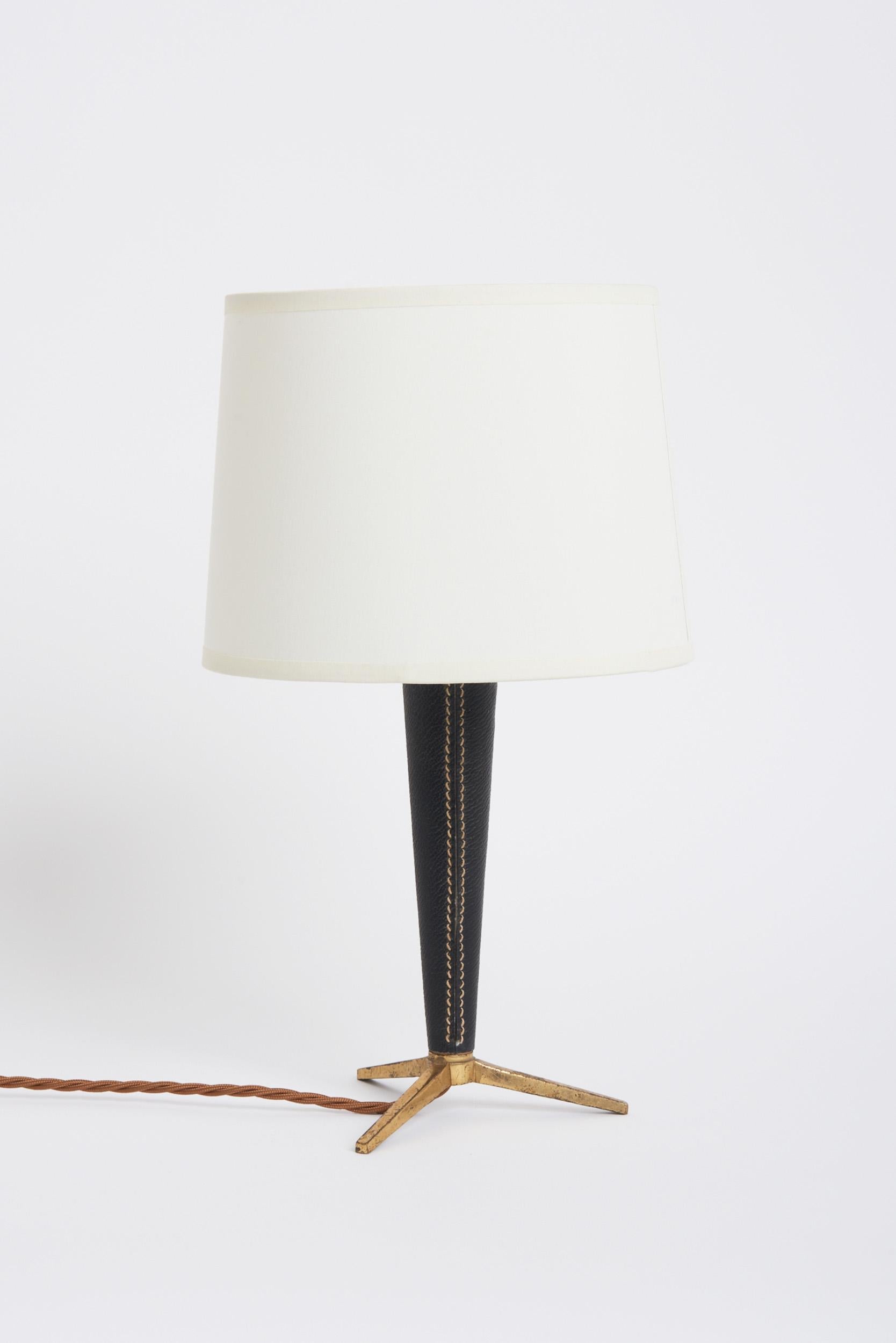 A saddle-stitched black faux lather and brass tripod table lamp.
France, third quarter of the 20th century. 
With the shade: 35 cm high by 20 cm diameter. 
Lamp base only: 25 cm high by 14 cm diameter.