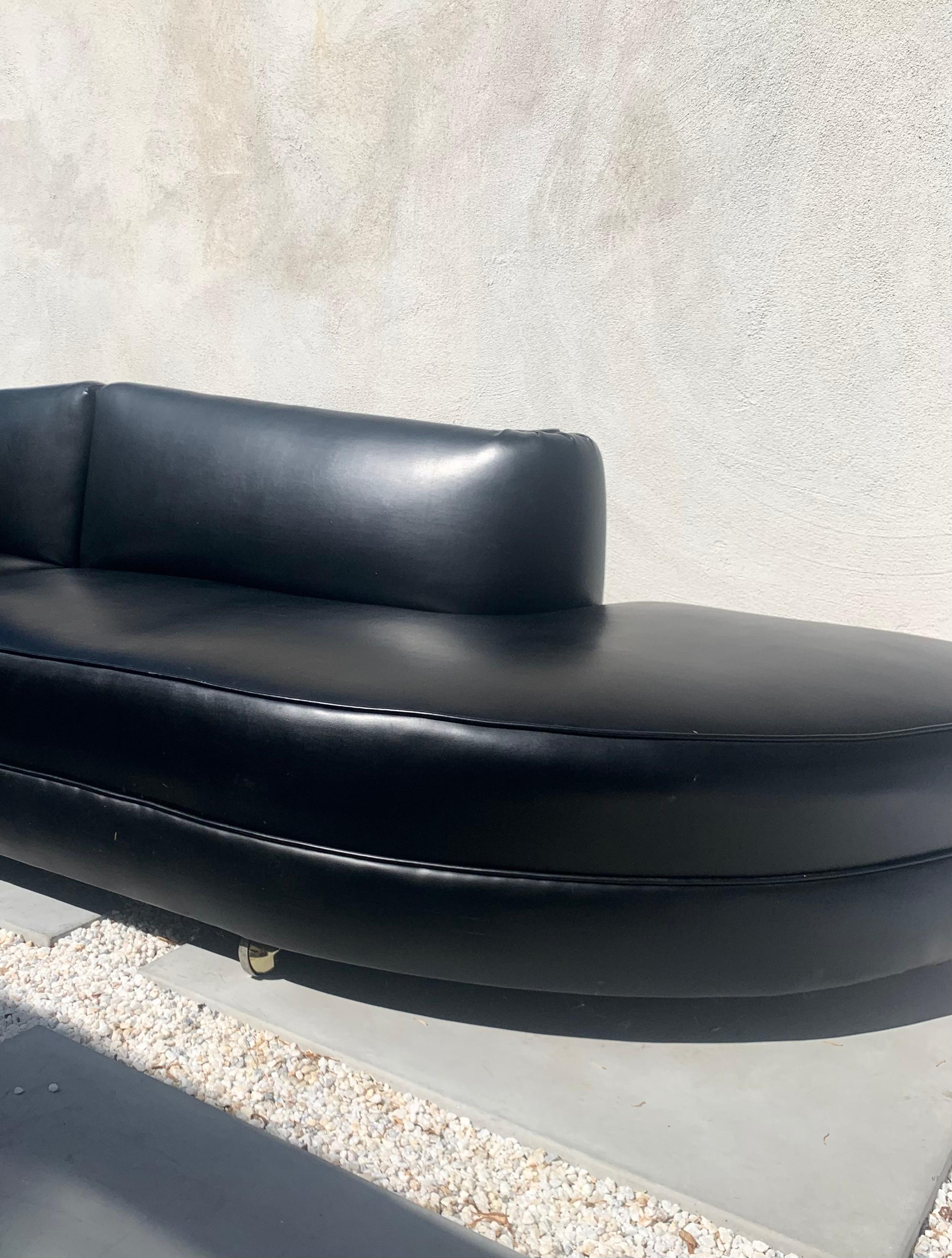 A black vinyl modular sofa sectional on brass casters, 1950s. Two sections that can be placed together or split as one desires. Featuring a thick double lip, this piece clearly exhibits Art Deco revival sensibilities whilst being a harbinger of