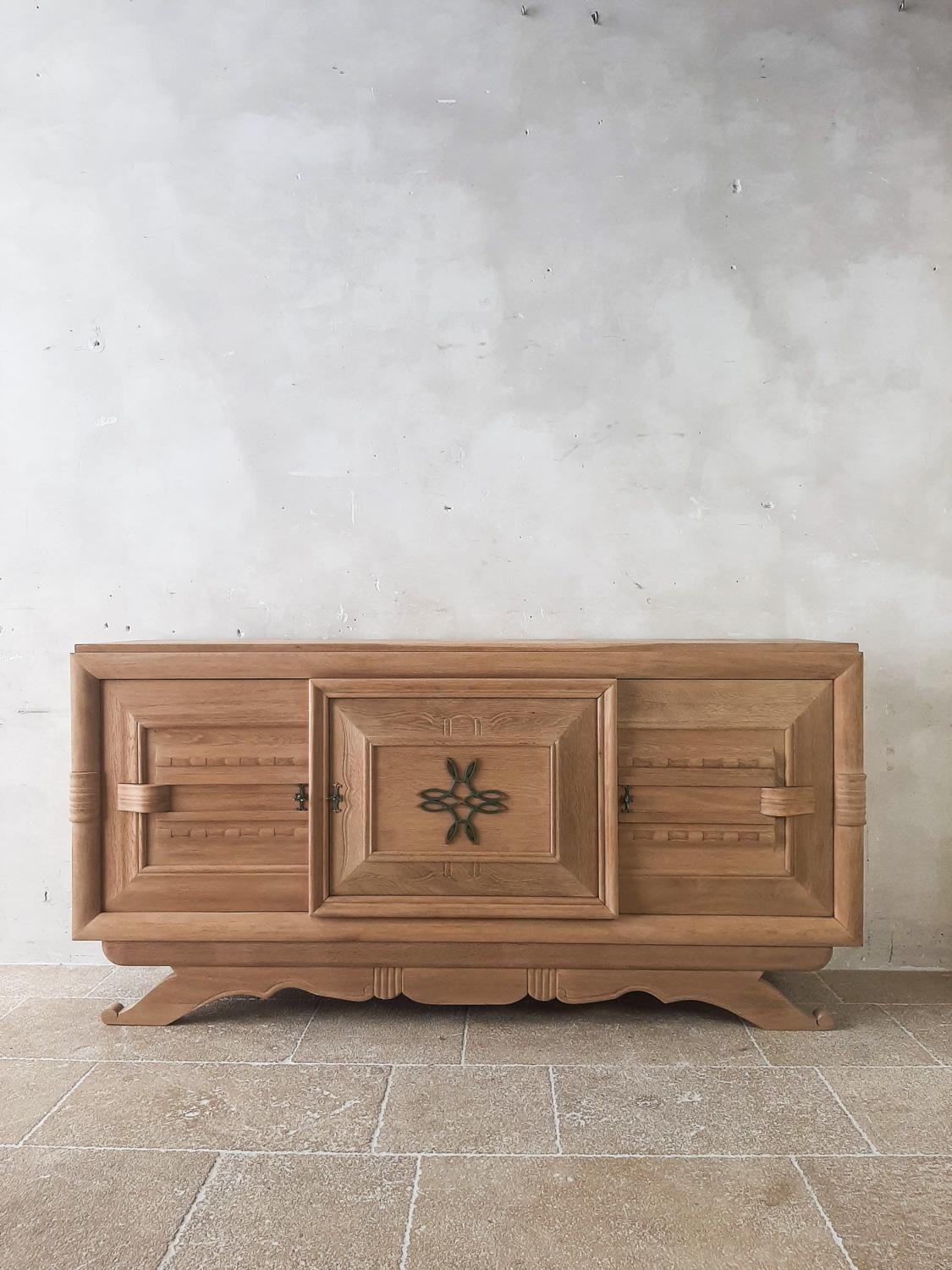 Mid-century bleached oak sideboard by Charles Dudouyt, 1940s-1950s. This credenza has a stunning design with 3 doors with subtle decorations in the wood, where the middle door is the focal point, with the brass decoration and its framed panel being