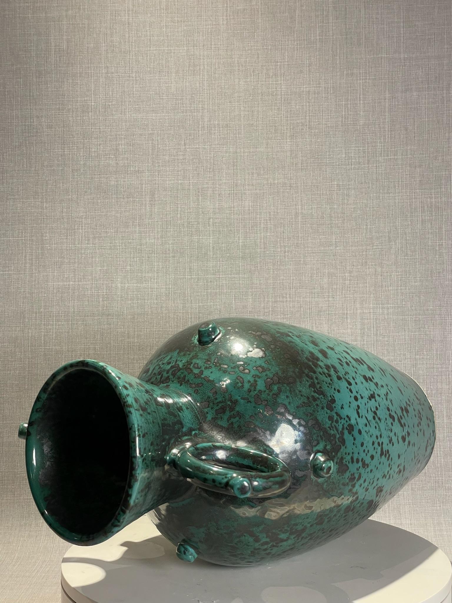 Questa grande urna in terracotta presenta un'accattivante smaltatura a macchie blu e nere che emana il fascino della metà del secolo scorso e dell'artigianato artistico. L'elegante silhouette ispirata all'anfora è caratterizzata da un corpo alto e