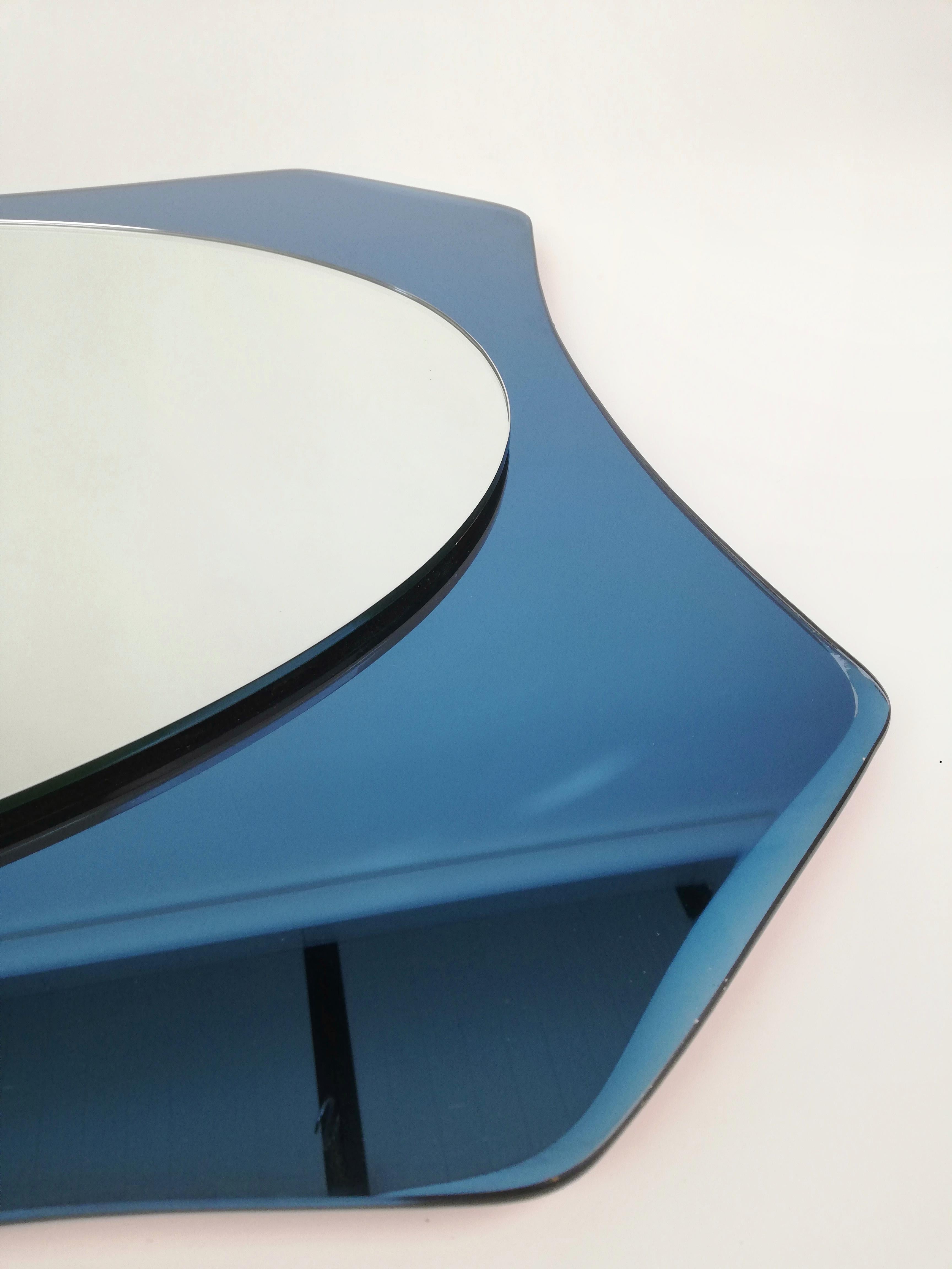 Italian-made mirror datable between the 1960s and 1970s.
The oval mirror is mounted on a frame of deep blue mirrored glass, whose supple lines form an octagon embellished along the sides by bevelled.
The style of the mirror makes it attributable to