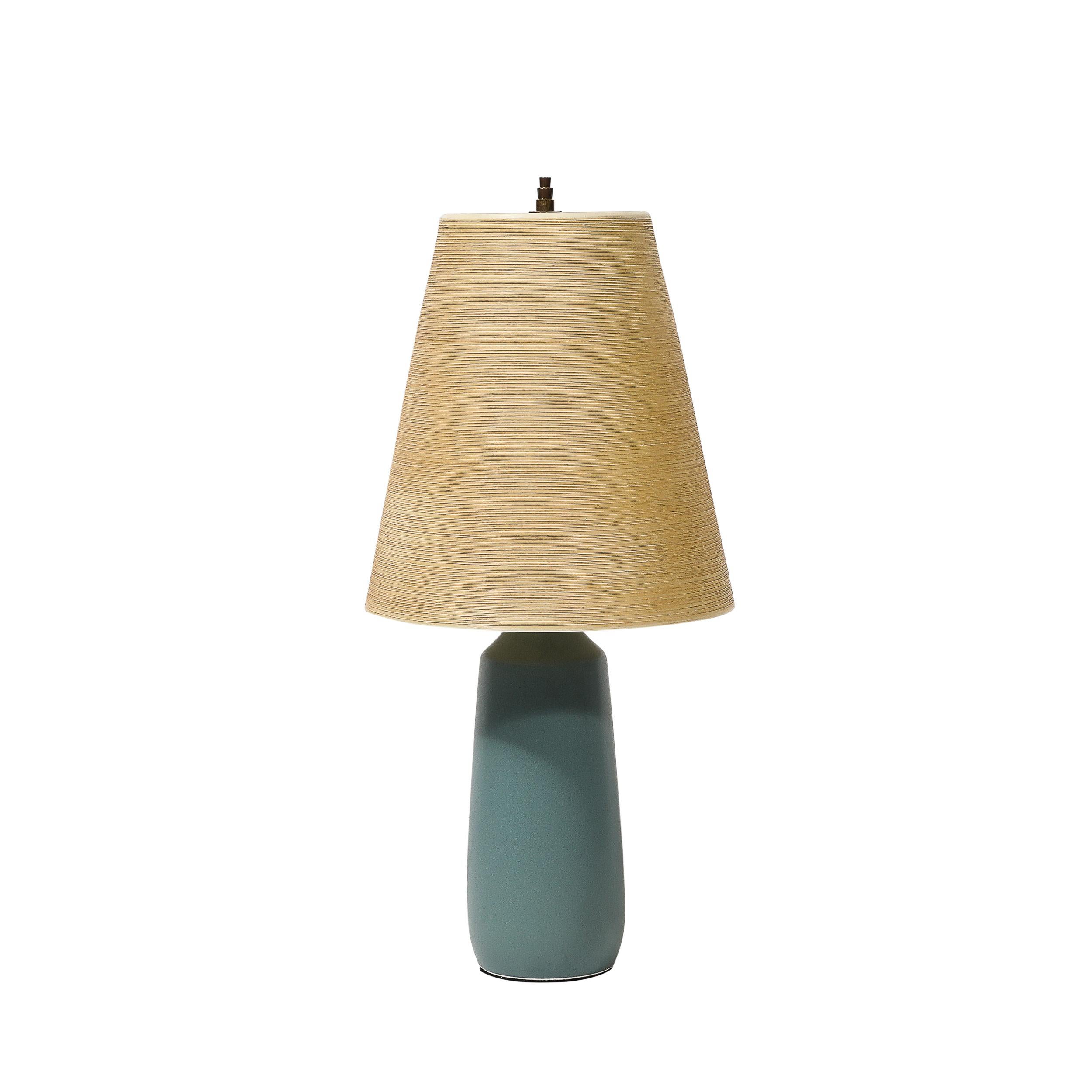 Designed by Lotte and Gunnar Bostlund in Canada around 1960, this pair of mid-century modernist table lamps features elegant blue ceramic bases paired with natural fiber shades. The harmonious blend of materials and the distinctive design are